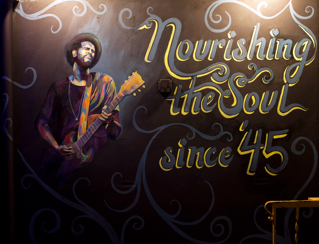 This mural was commissioned with the intention of reviving the energy within the environment. This wall is approximately 8 feet by 8 feet and is across from the main stage. My intentions were to emulate the feeling of a musician in the room when no one is playing. With the placement of the figure and the lettering, this wall functions well as a backdrop for customers and tourists to take photos with.