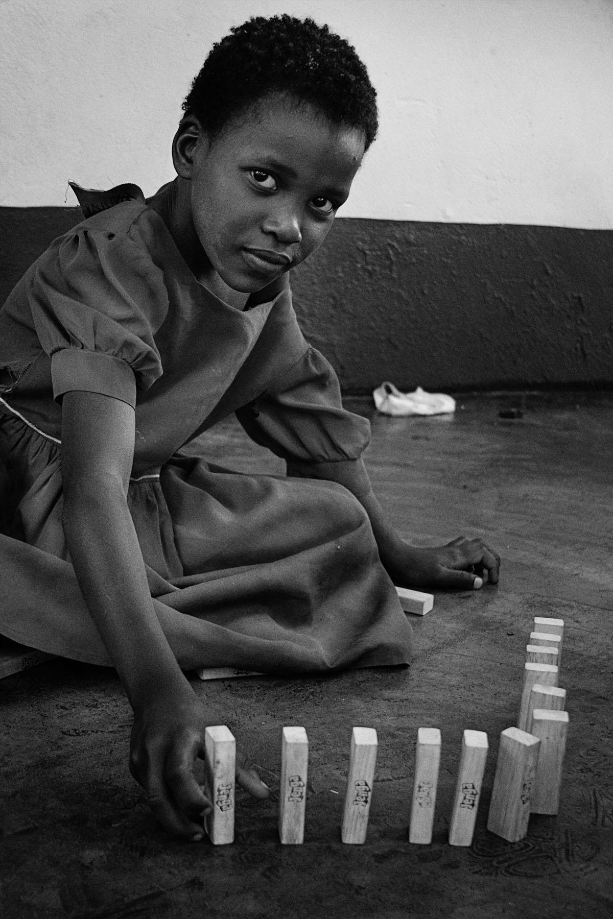 In the township of Chinotimba, Zimbabwe, a local woman Sima Moyo has opened her doors to some of the areas most needy children. The children, some HIV+, some disabled, some homeless, some not in school but mostly orphans are helped by the The Rose of Charity she has set up. They come to her home a few times a week for love and attention and a sense of security and belonging, as well as food and drink and sometimes even chocolate cake. The orphanage encourages them to go to school helping them raise funds, even find sponsors to help pay for their education in the hope of giving them the choices in life we so often take for granted. The charities biggest aim is to help each child to become self-sufficient and see a future they can look forward to and with the growing of a vegetable garden, the formation of a drumming group, a theater group and now even a majorette troupe that is exactly what the children can now see.