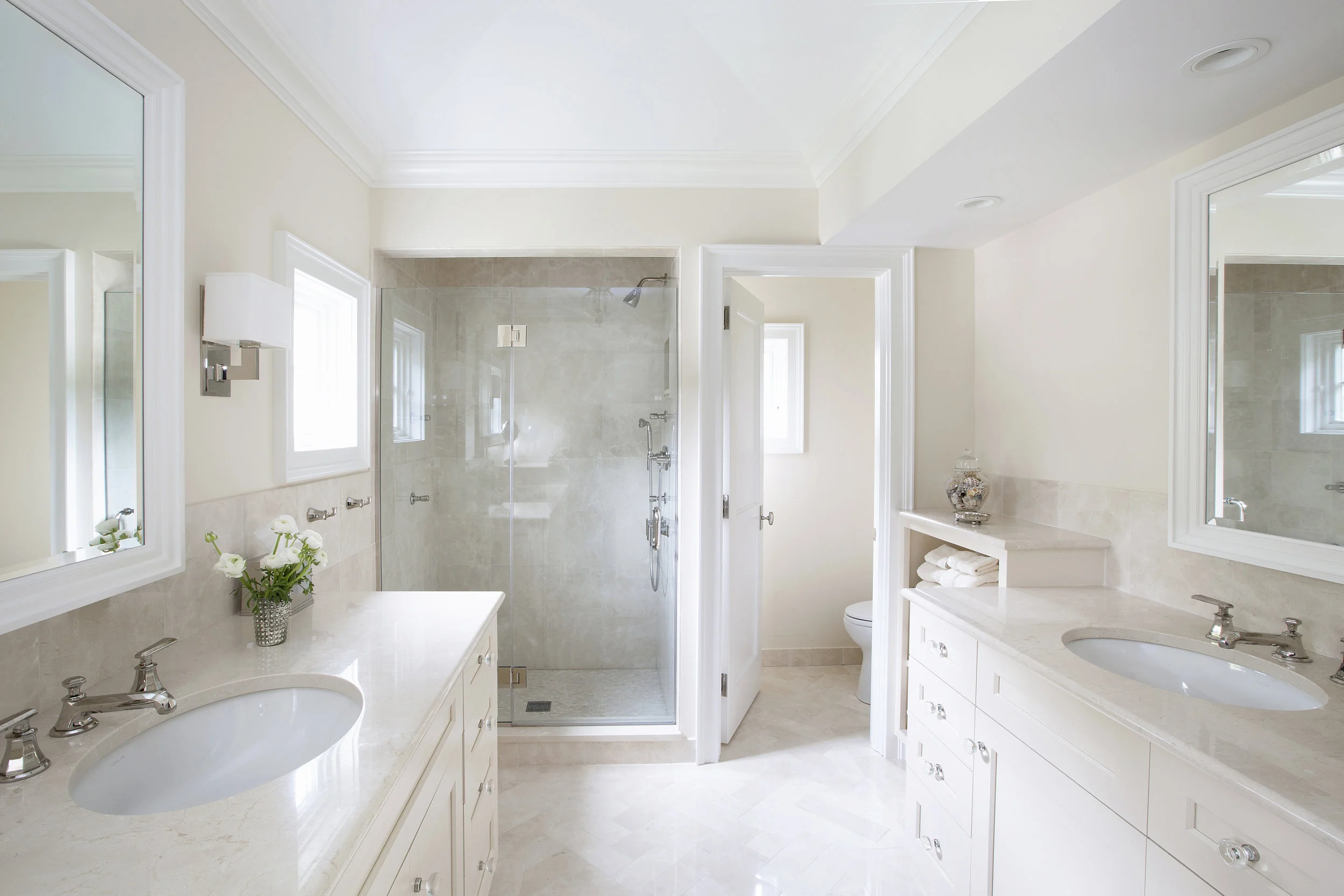 The palette of creamy neutrals carries over into the master bath, where our team installed Crema Marfil marble tile in a herringbone patter on the floor. The same marble covers the vanities and the walk-in shower.