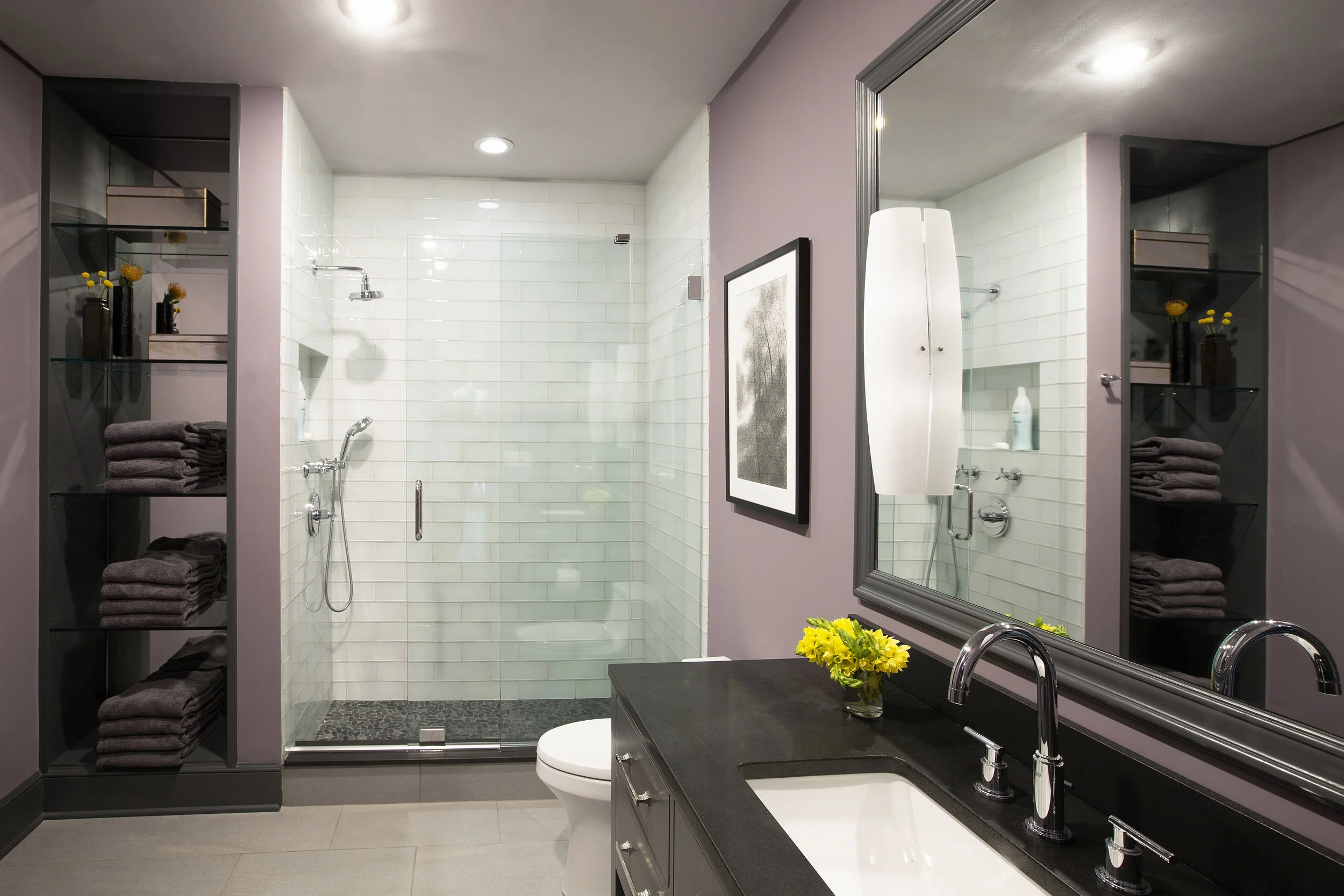 Honed black granite surfaces echo the countertops in the kitchen and butler’s pantry. Glass tile brightens the shower area, and practical gray ceramic flooring tile continues the neutral color scheme of the rest of the house.