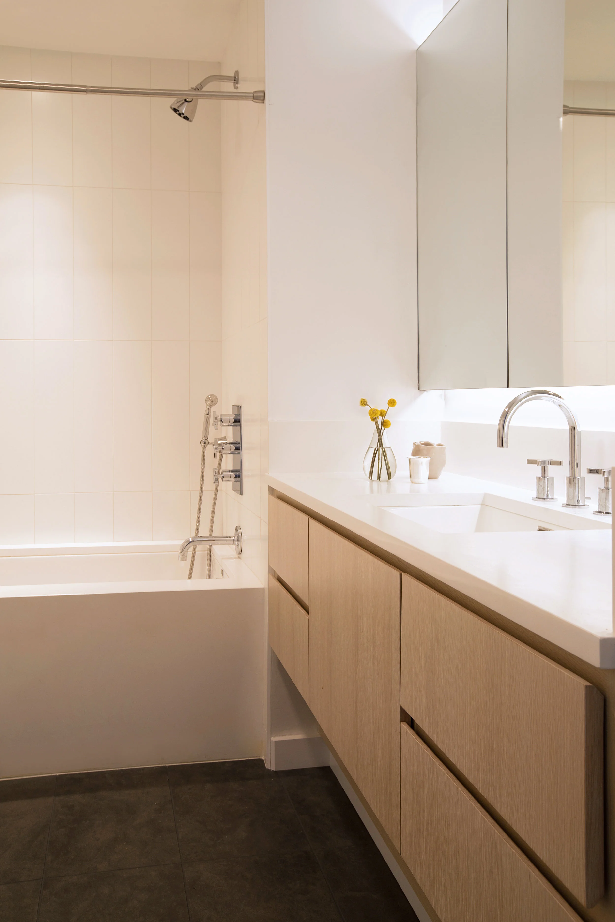 In the kids bath gray limestone flooring is the same material used throughout the other rooms of the house, including the kitchen and dining area. A wall-to-wall surface mounted medicine cabinet provides plenty of storage.