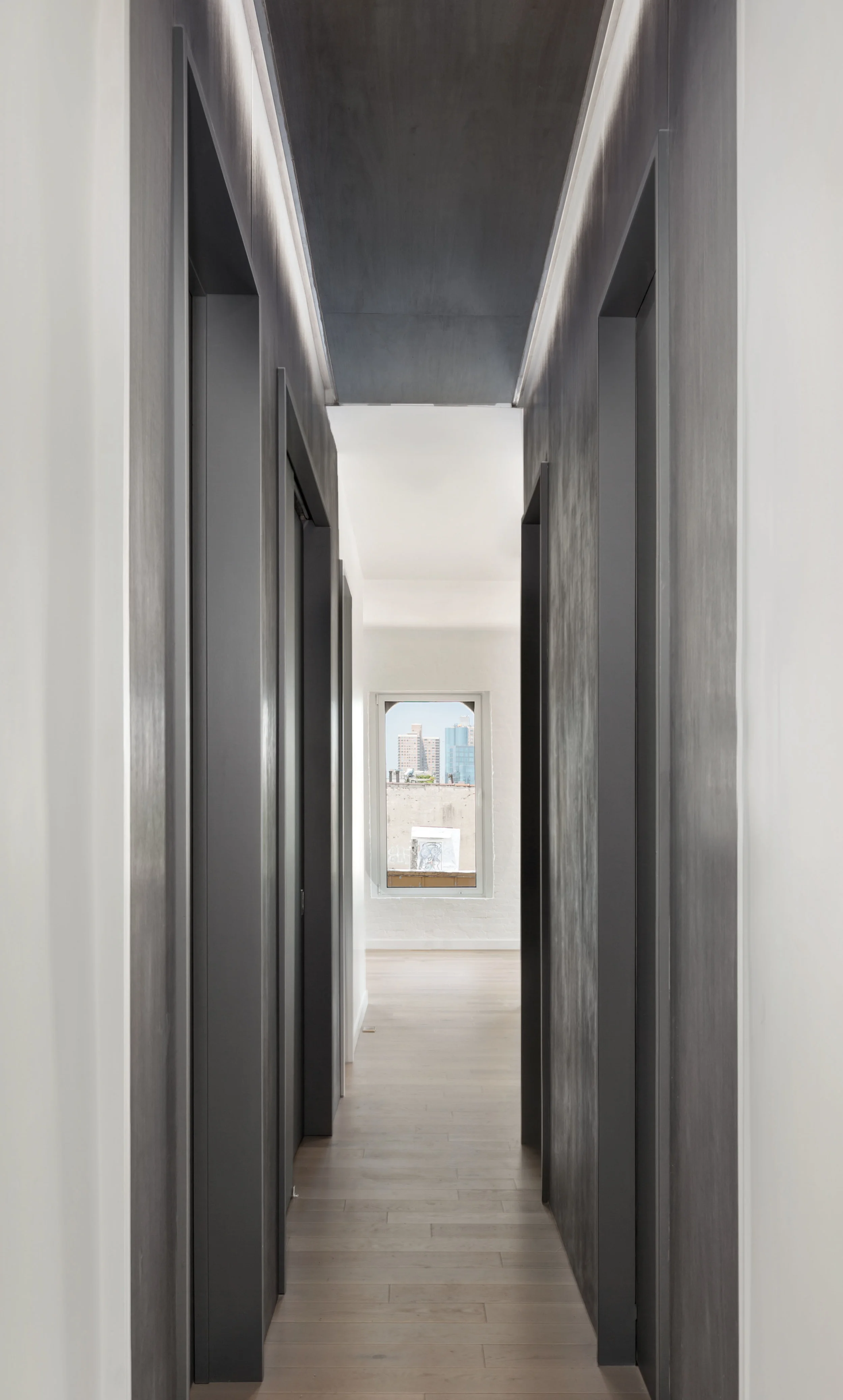 Long entry corridor is foreshortened with gray wood veneer wood and lighting feature, leading you into the open kitchen/living areas.
