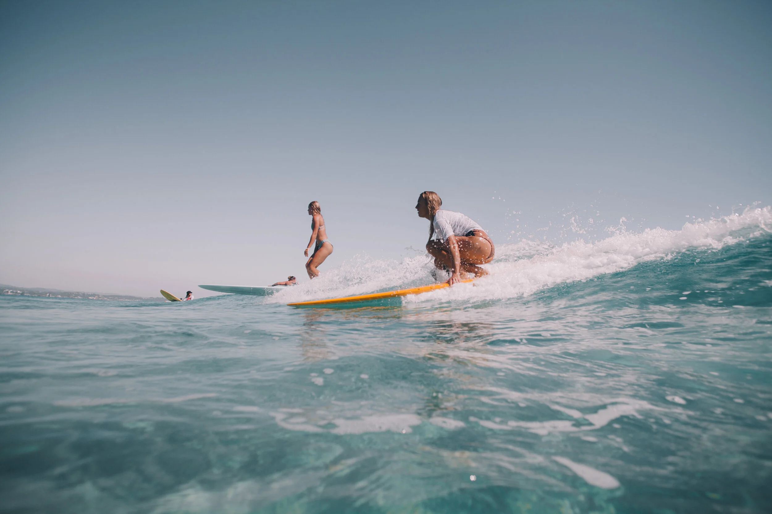 An unknown surfer demonstrating a great pop-up without first getting to her knees. Notice how she still holds her rails until after her feat are firmly planted. And @maddyhoffmann riding gracefully in the back ground. PC: @amypearlphoto