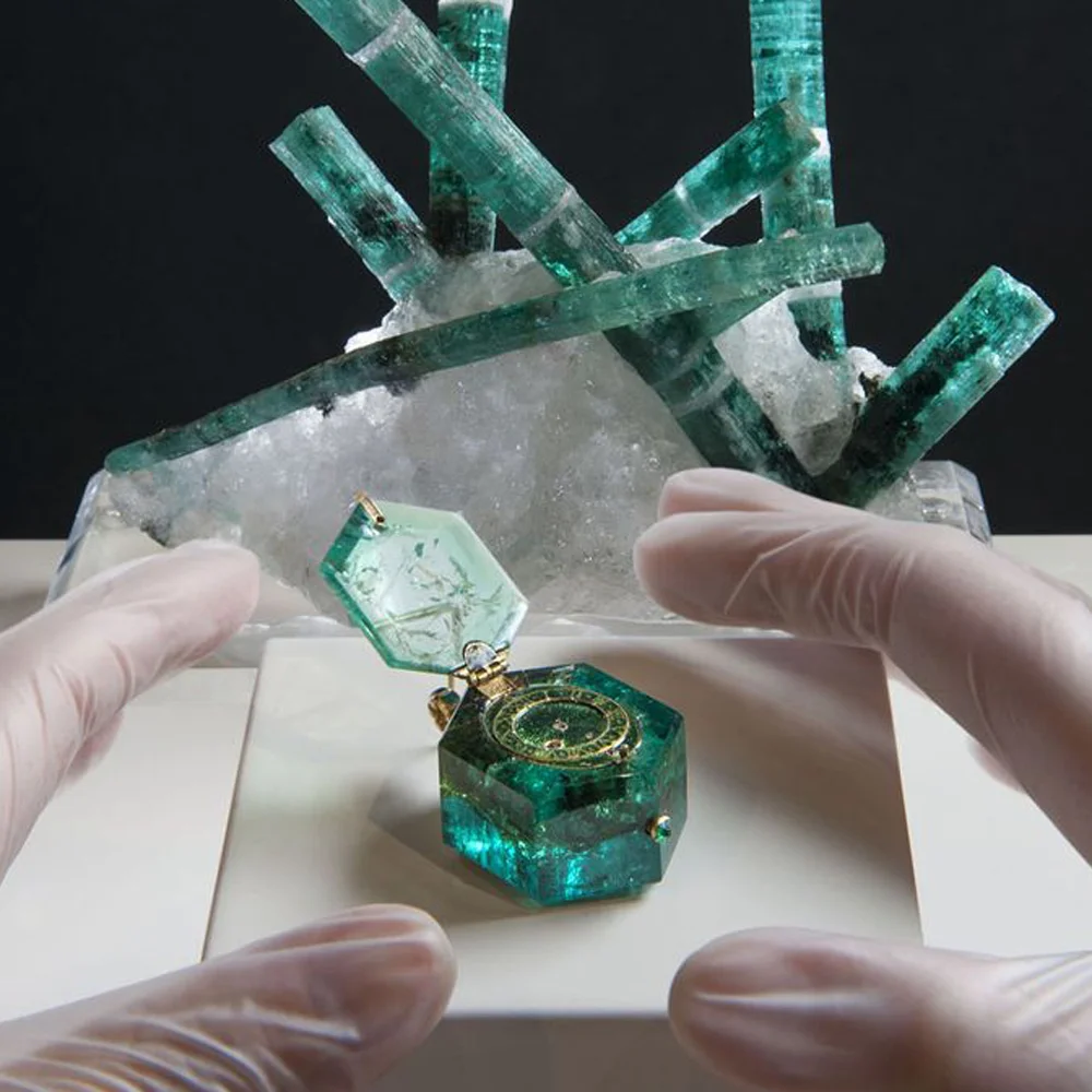 Old vs. New: 16th century watch found in the Cheapside hoard carved from a single emerald, displayed next to a Zambian emerald crystal.