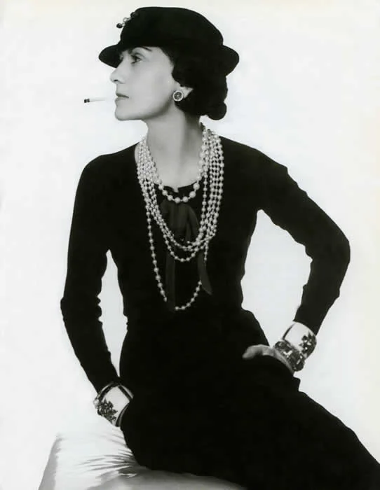 Coco Chanel wearing her trademark pearls, Verdura cuffs and signature cigarette.