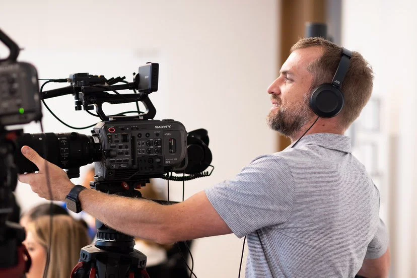 Video camera operator filming with Sony 4K camera, wearing headphones, indoors