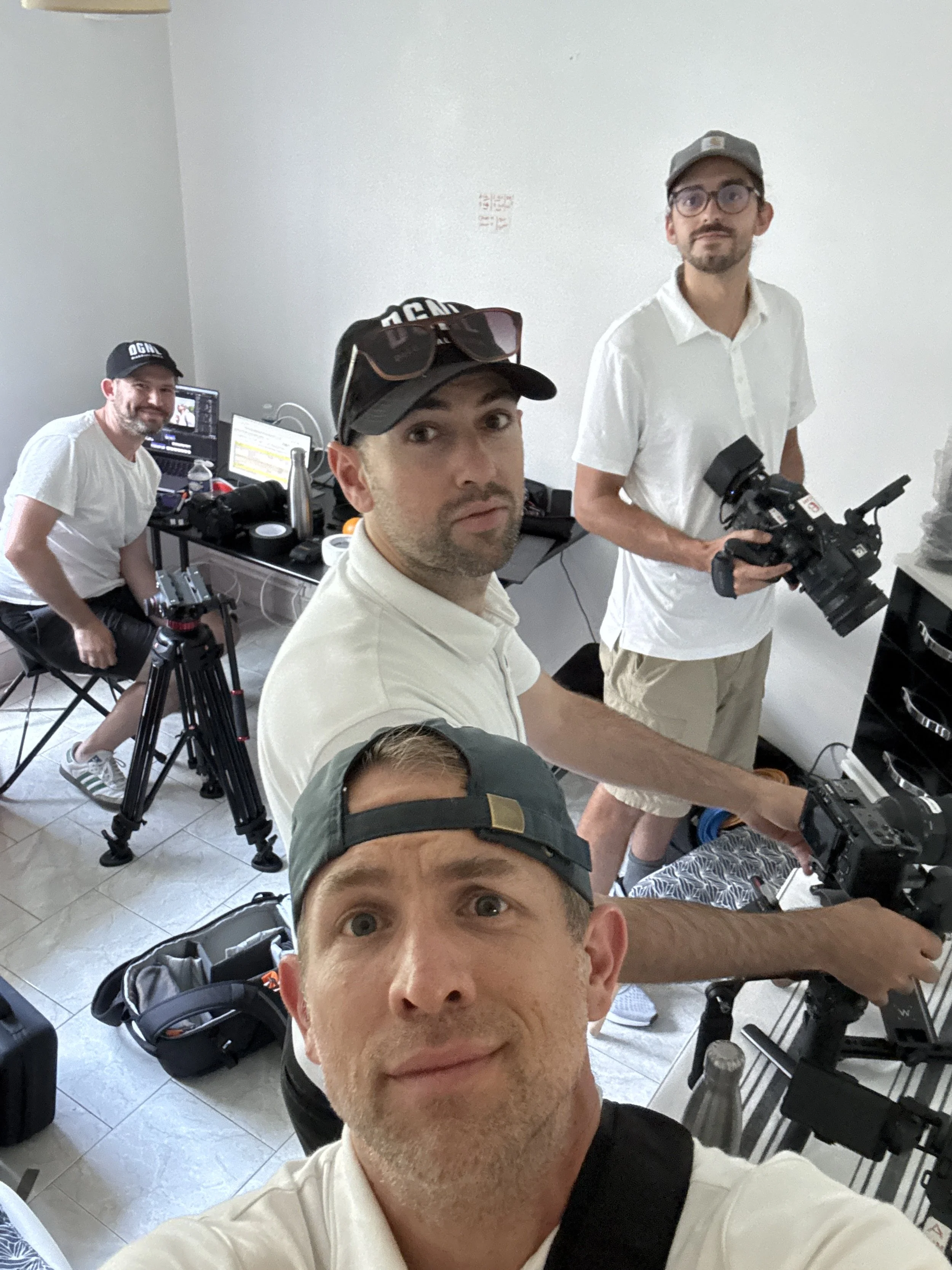 Group of four men in a room with camera equipment and computers, taking a selfie.