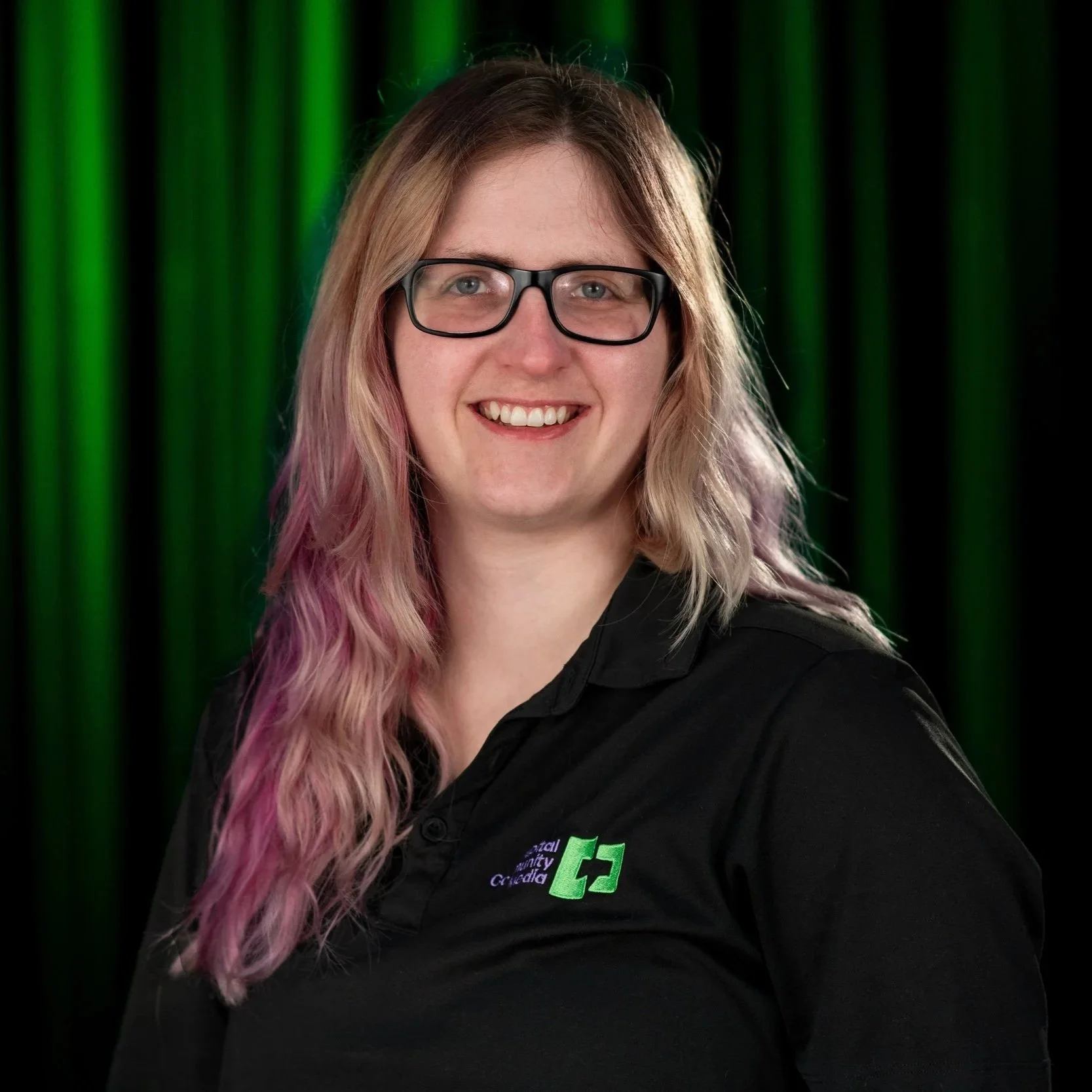 A Woman in black shit with Capital Community Media Staff on it with a back and Green background.