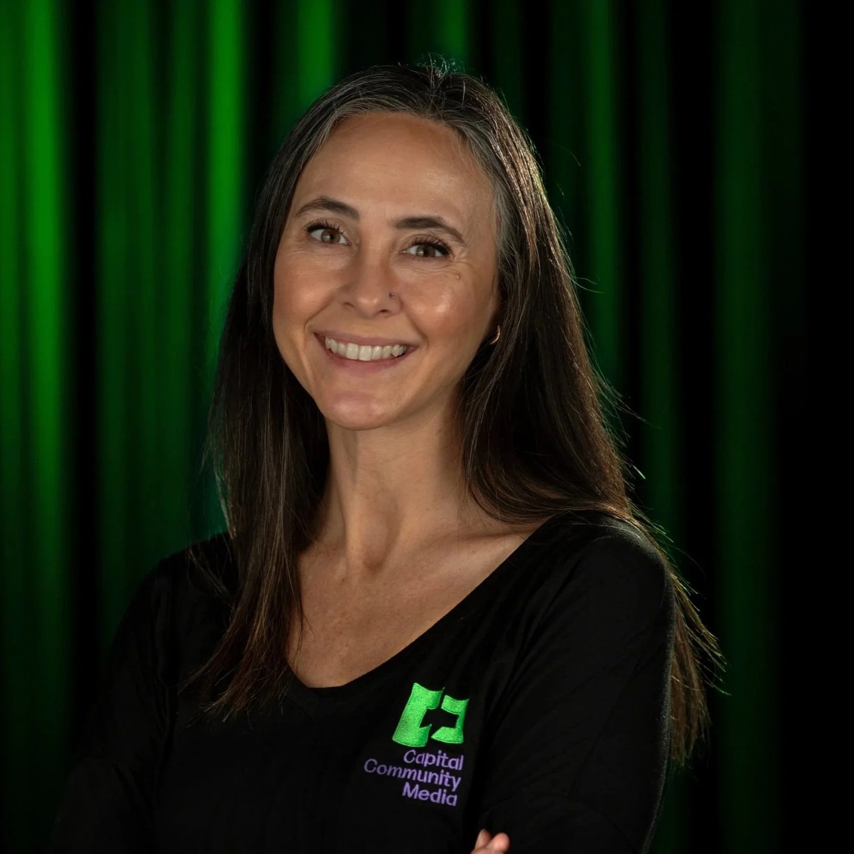 A Woman in black shit with Capital Community Media Staff on it with a back and Green background.