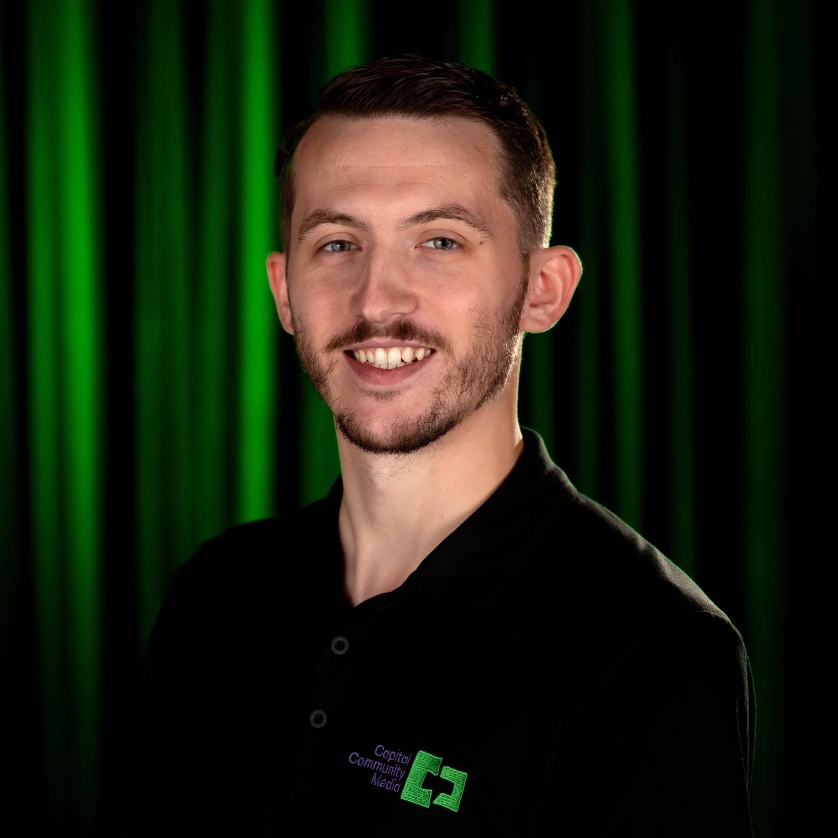 A man in black shit with Capital Community Media Staff on it with a back and Green background.