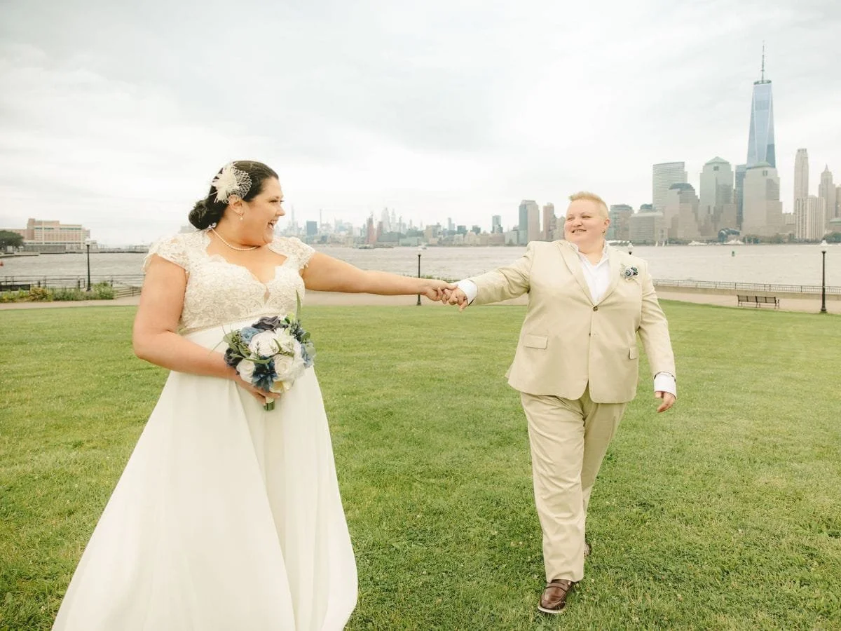 Couple holding hands and walking together during their Liberty State Park elopement with the New York City skyline behind them