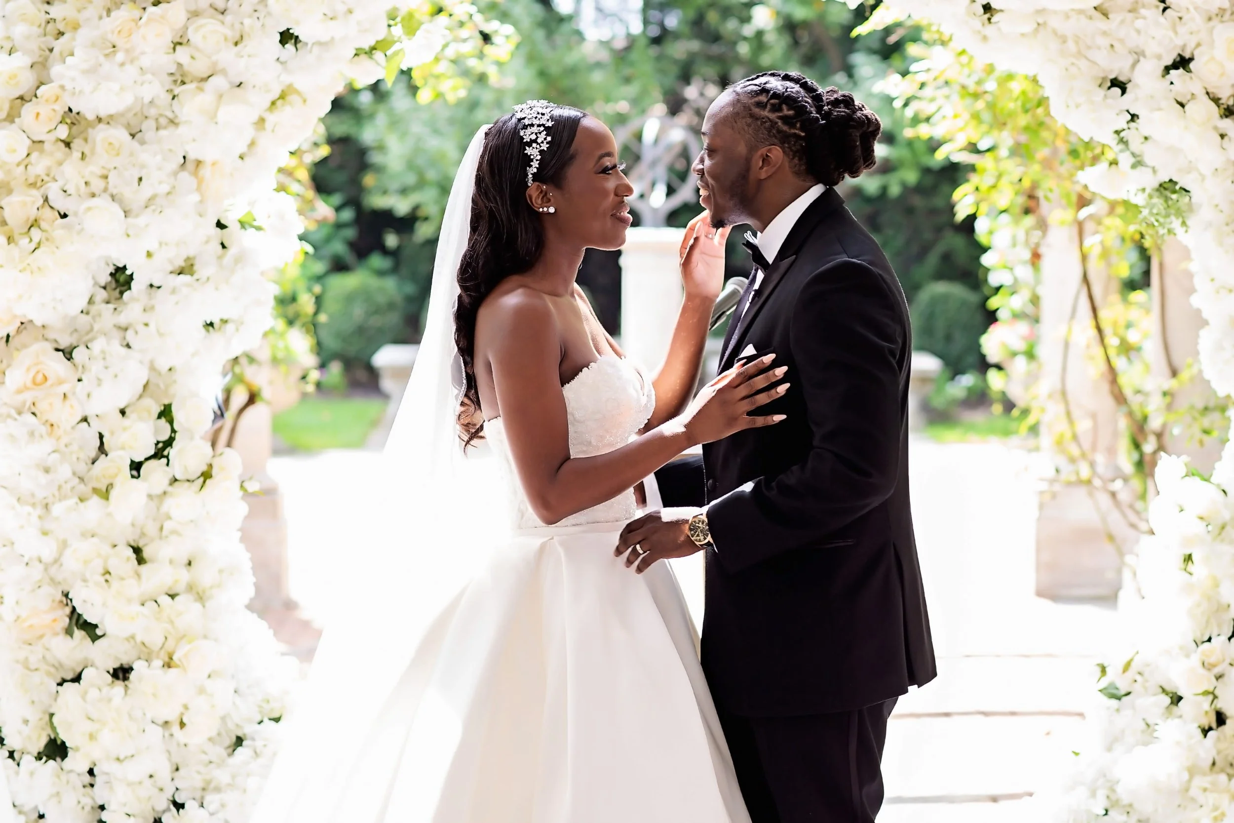 Bride in a strapless mermaid gown and long veil holding hands with her groom in a black tuxedo in a hallway lined with crystal sconces at The Estate at Florentine Gardens in River Vale, NJ