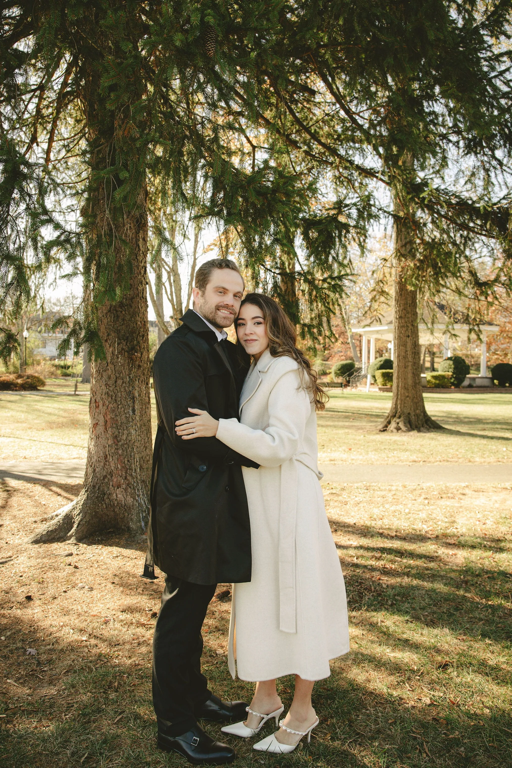 Charles and Fernanda embrace under tall evergreen trees on their elopement day at Mindowaskin Park in Westfield, NJ