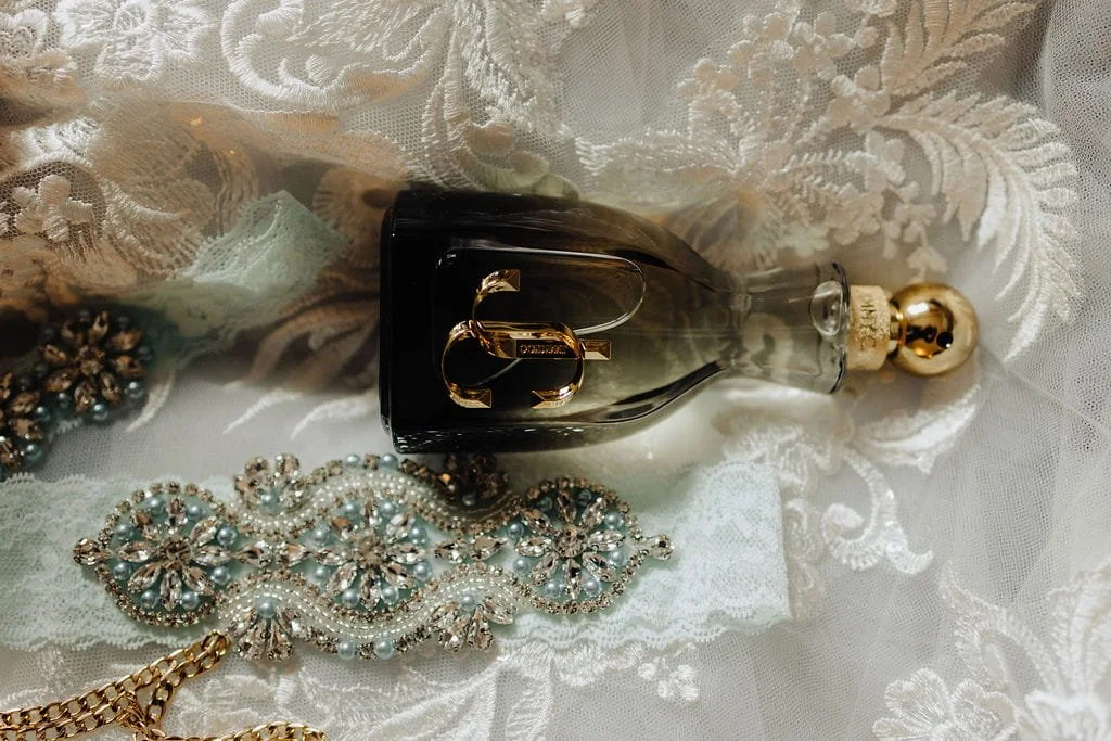 Kristie’s bridal perfume and jeweled accessories photographed with the lace details of her wedding dress.