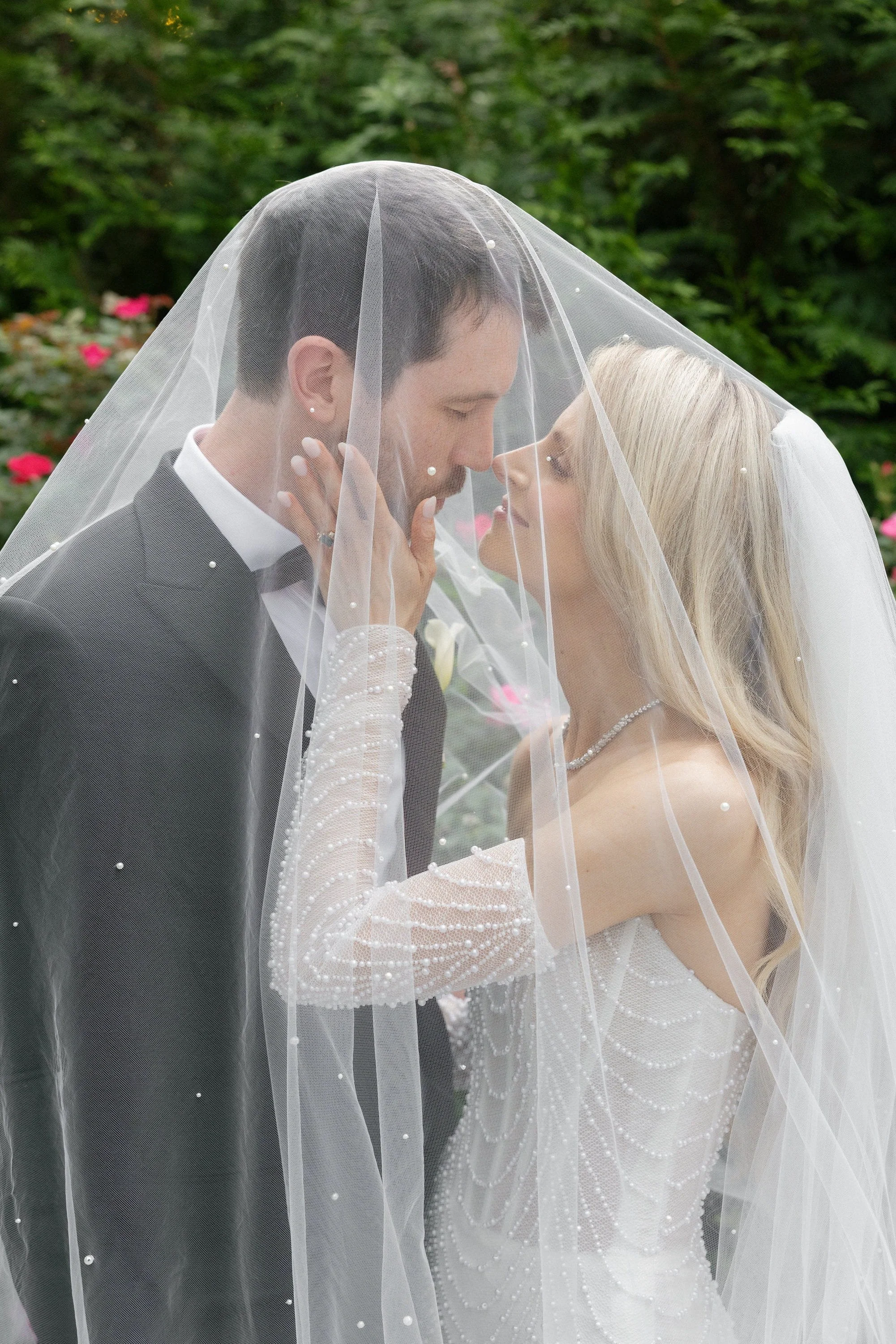 Caroline and Brett kissing beneath her pearl-detailed veil in the gardens at Florentine Gardens in River Vale, NJ