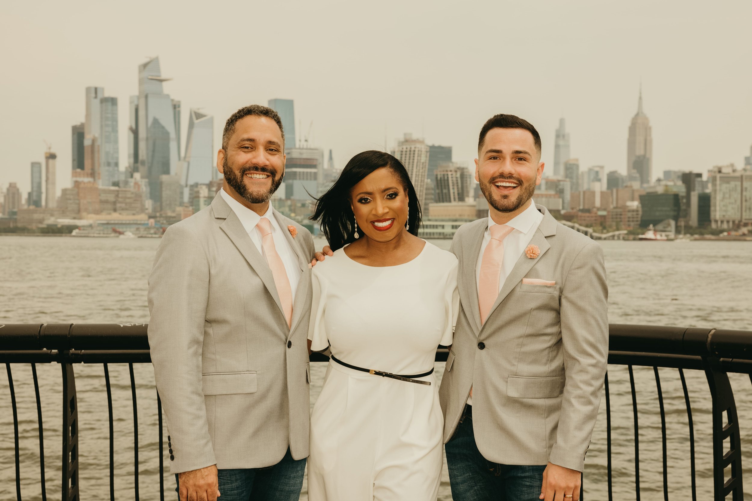 LGBTQ+ couple with New Jersey wedding officiant Aretha after their intimate elopement at Pier A in Hoboken, NJ with the Manhattan skyline in the background.