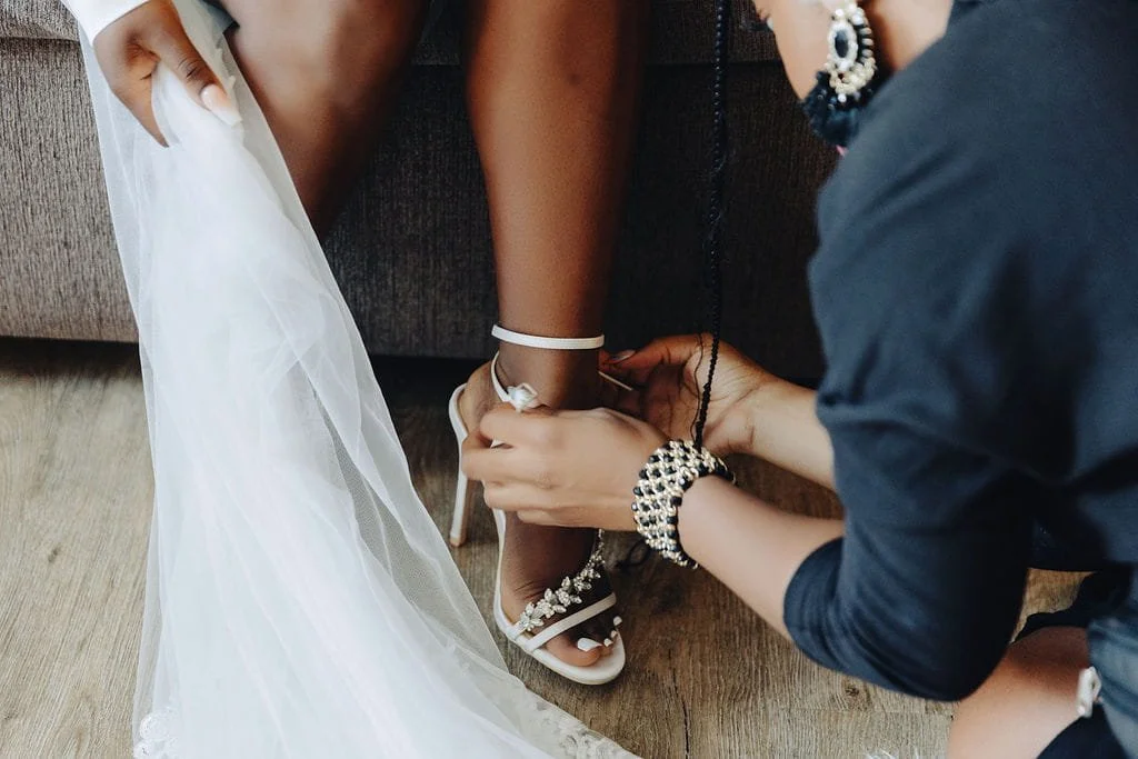 A member of the wedding party helps fasten Kristie’s bridal shoe as she gets ready for the ceremony.