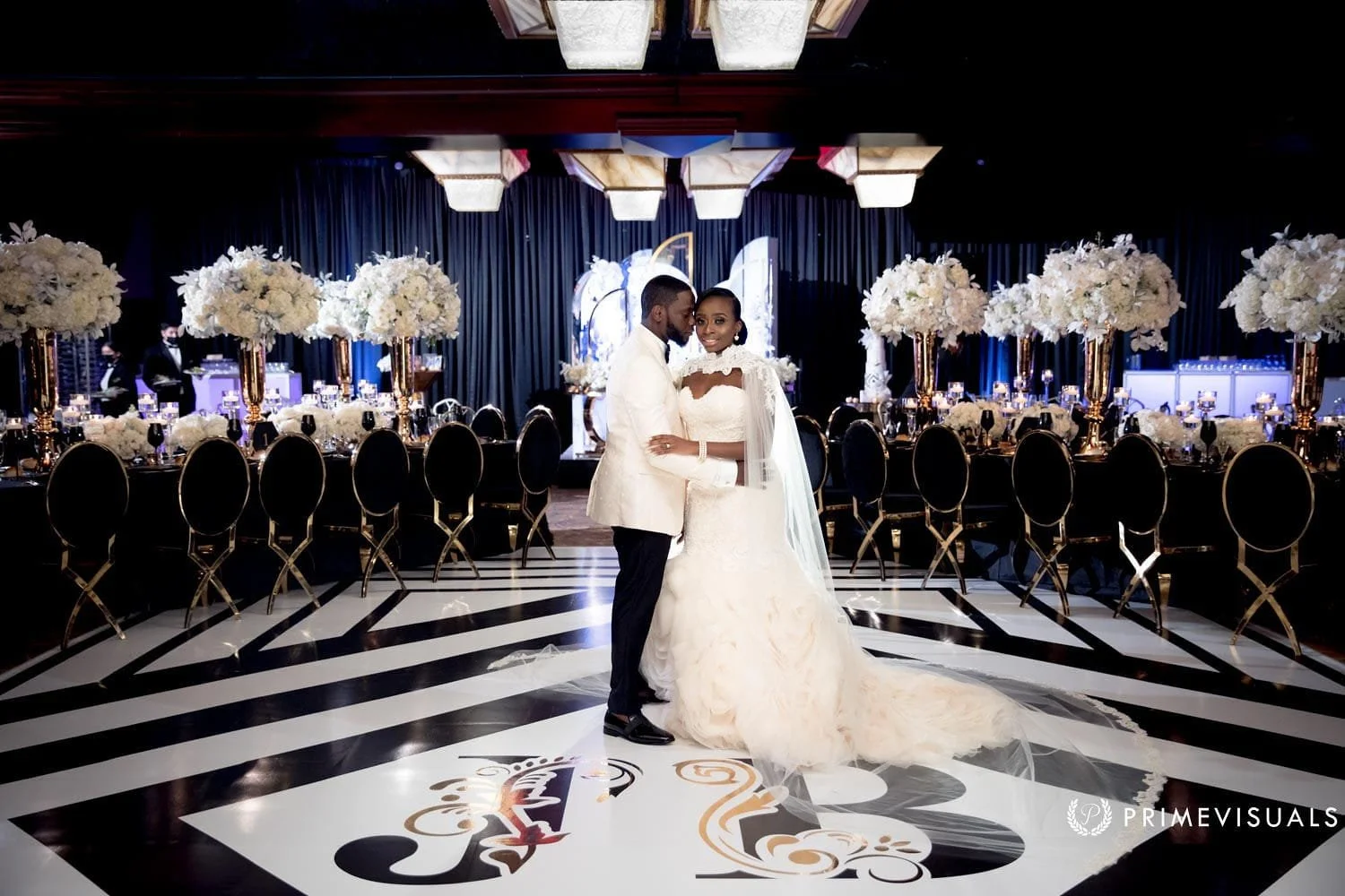 Nequila and Yvener embrace on a black and white monogrammed dance floor in a ballroom filled with tall white floral centerpieces