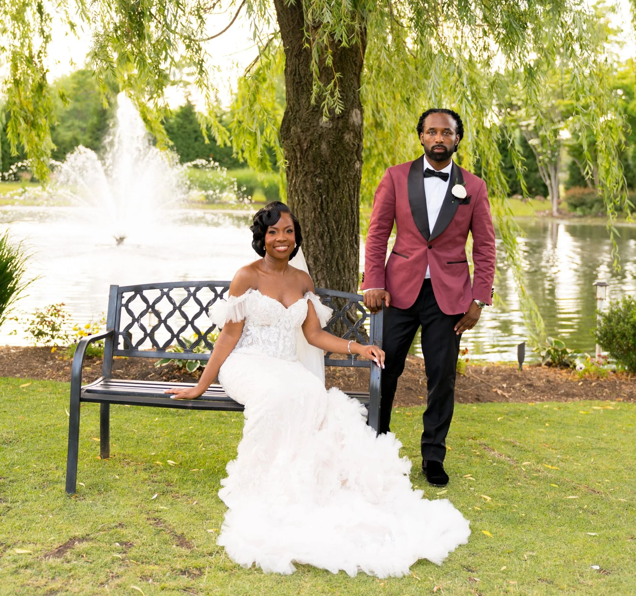Sarah and Courtney pose beneath a willow tree beside a pond with a fountain on their wedding day