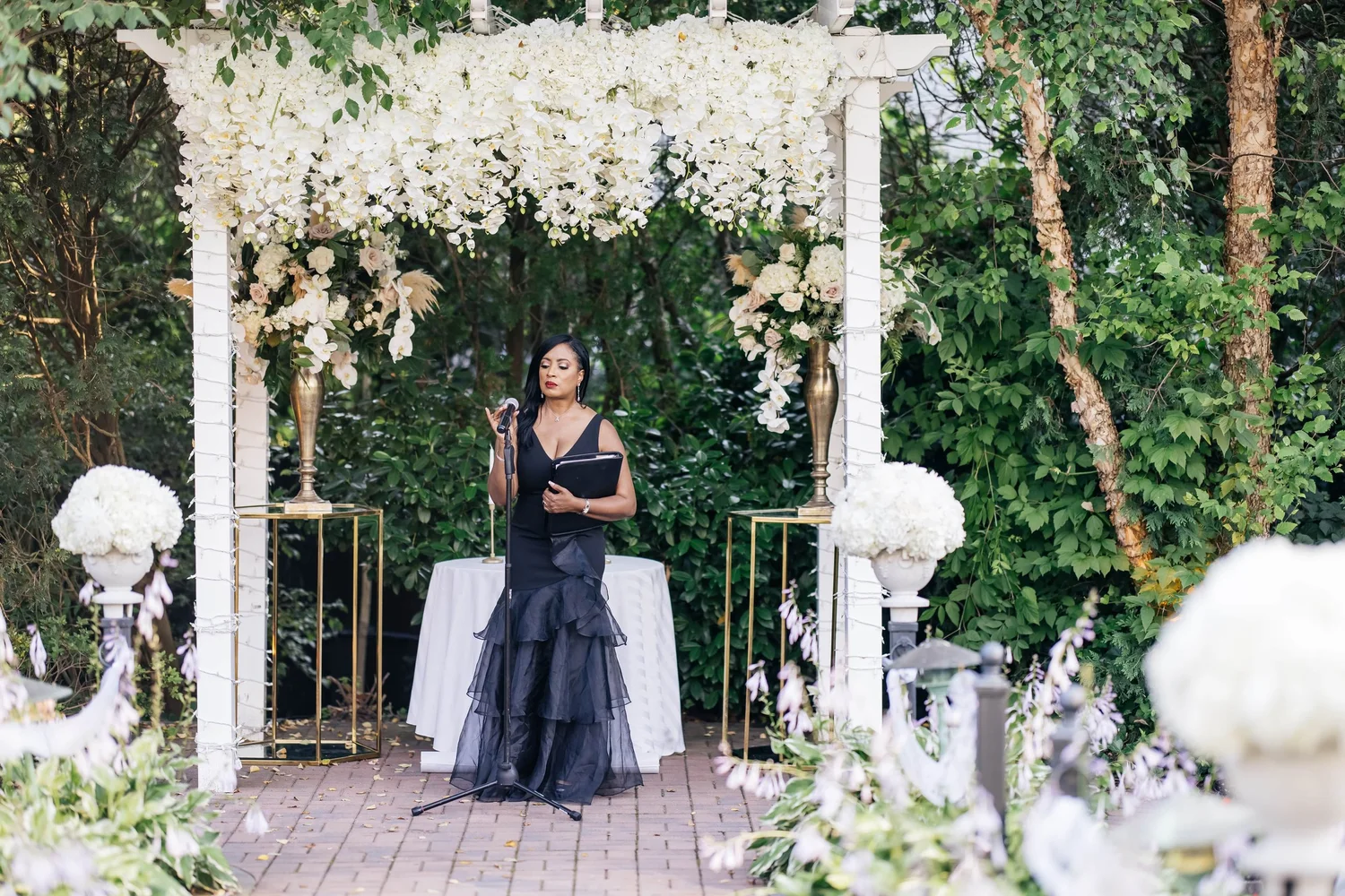 Aretha officiating in a tiered black organza gown under a floral pergola