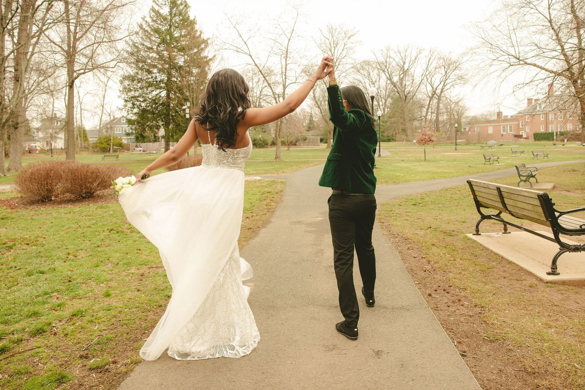 Bride and groom walking hand in hand down a park path at Mindowaskin Park, raising their joined hands in celebration.