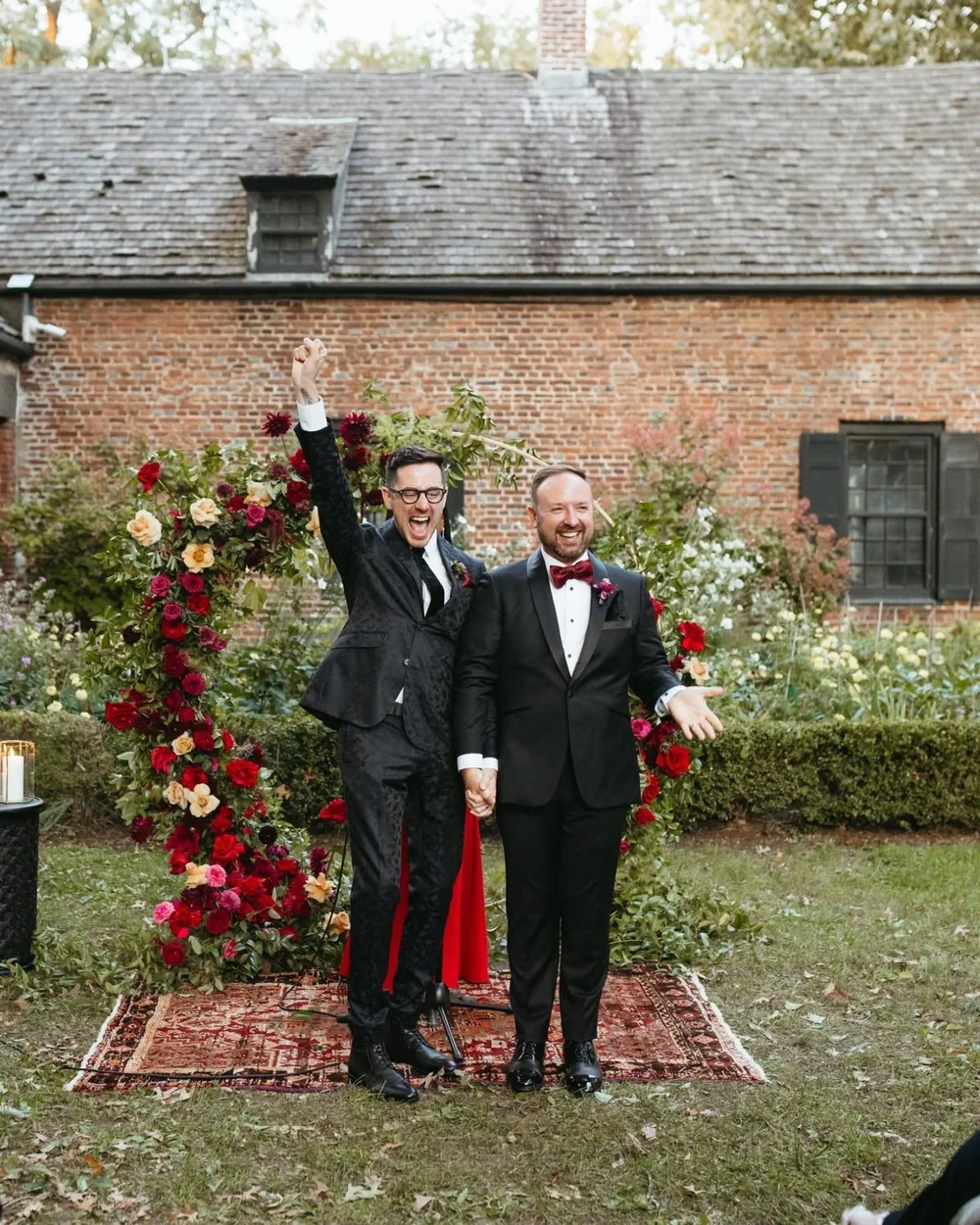 Matthew and Corey celebrate in front of a red floral arch at Senate Garage in Kingston, NY