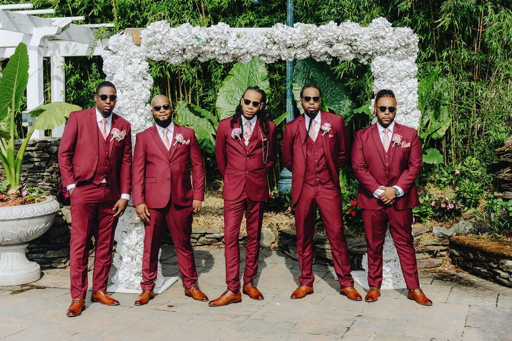 Gillon’s groomsmen posing together in burgundy suits at Sand Castle in Franklin Square, NY