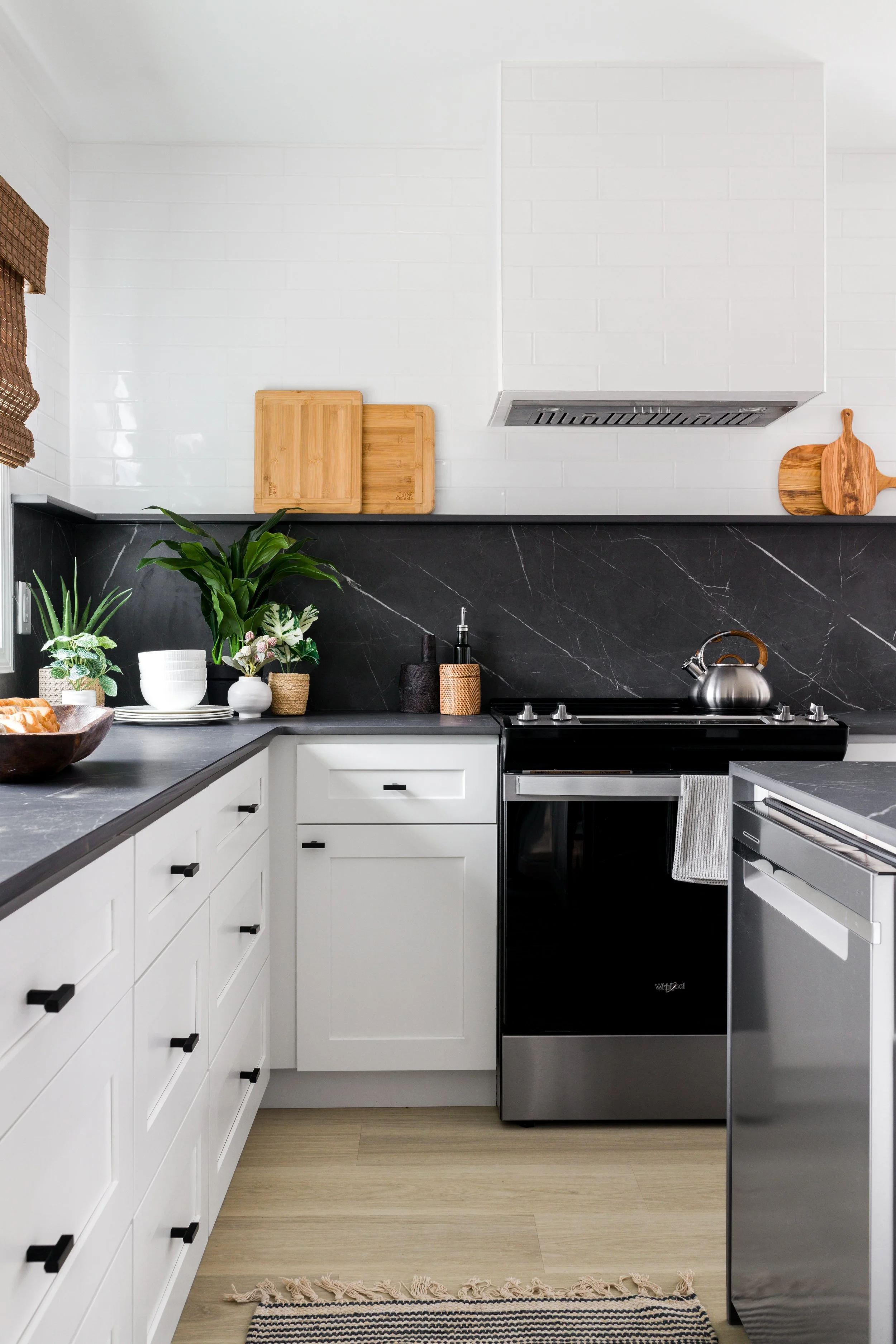 Modern kitchen with white shaker cabinetry, black stone backsplash, stainless range, and integrated dishwasher.