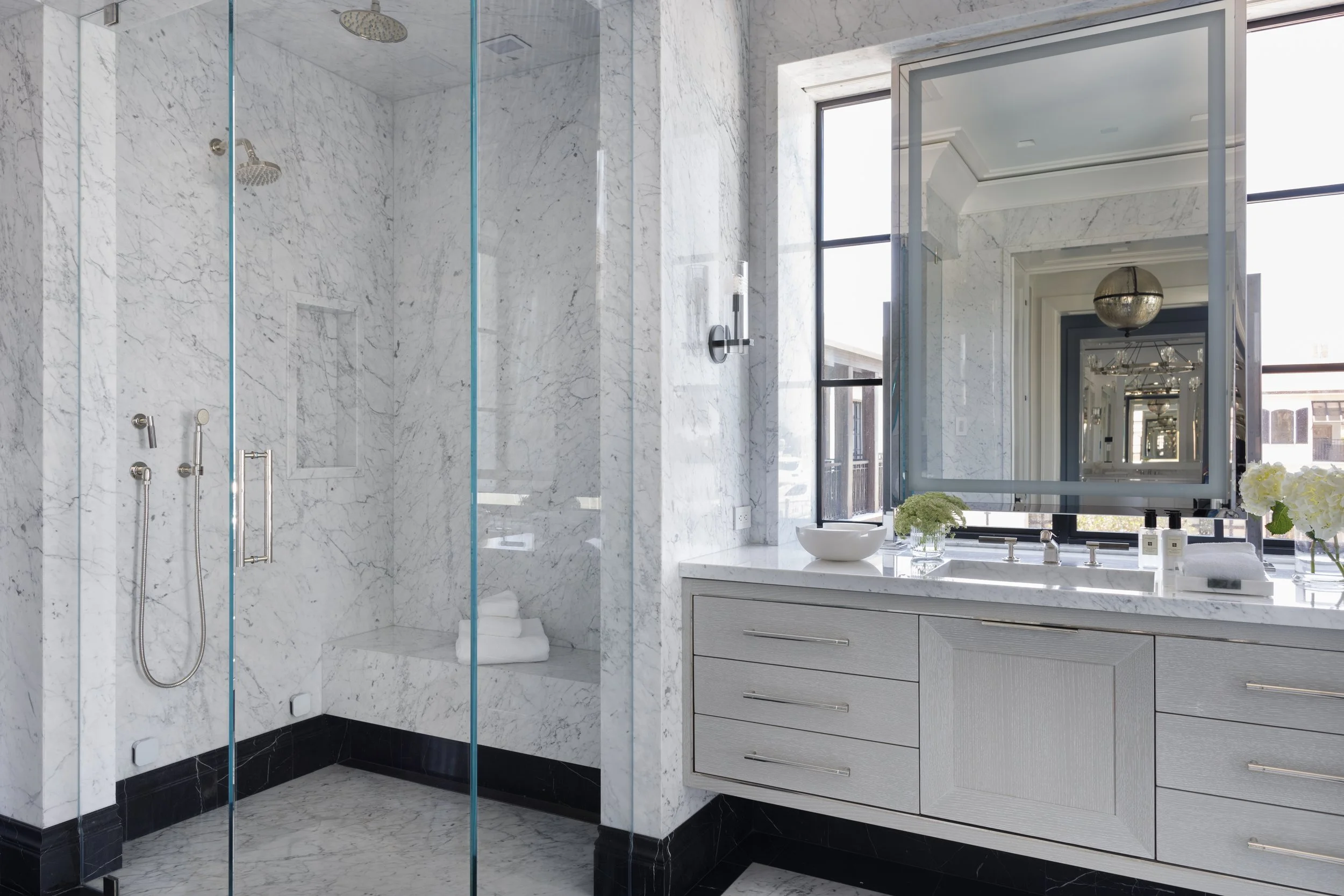 Marble primary bathroom with glass-enclosed walk-in shower, floating vanity, and oversized mirror.