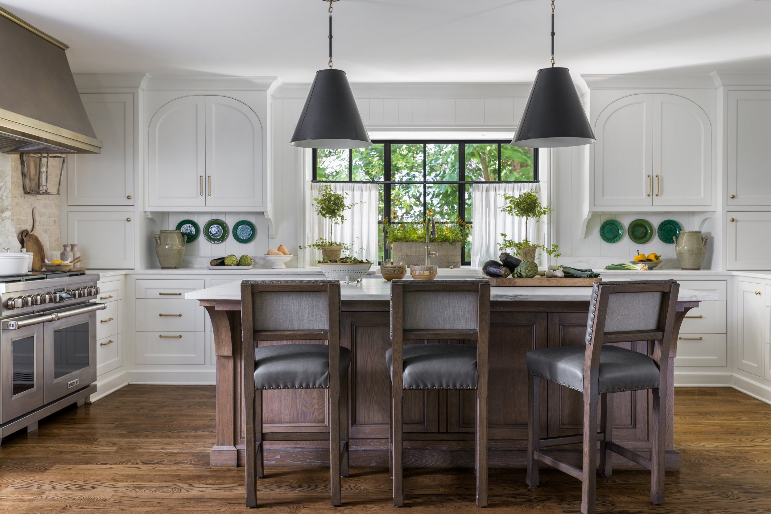 Bright kitchen with custom wood island, white cabinetry, black pendant lighting, and large window over the sink.
