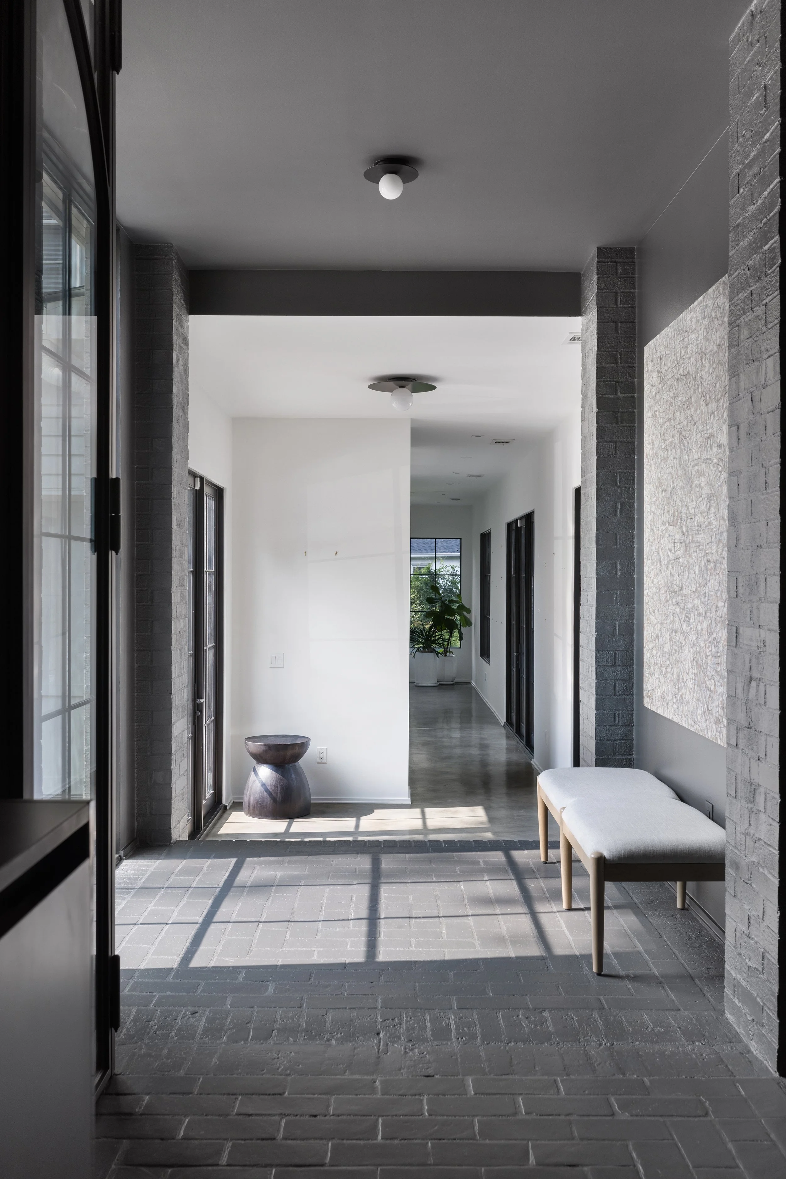 Minimal residential hallway with brick flooring, soft natural light, and sculptural seating.