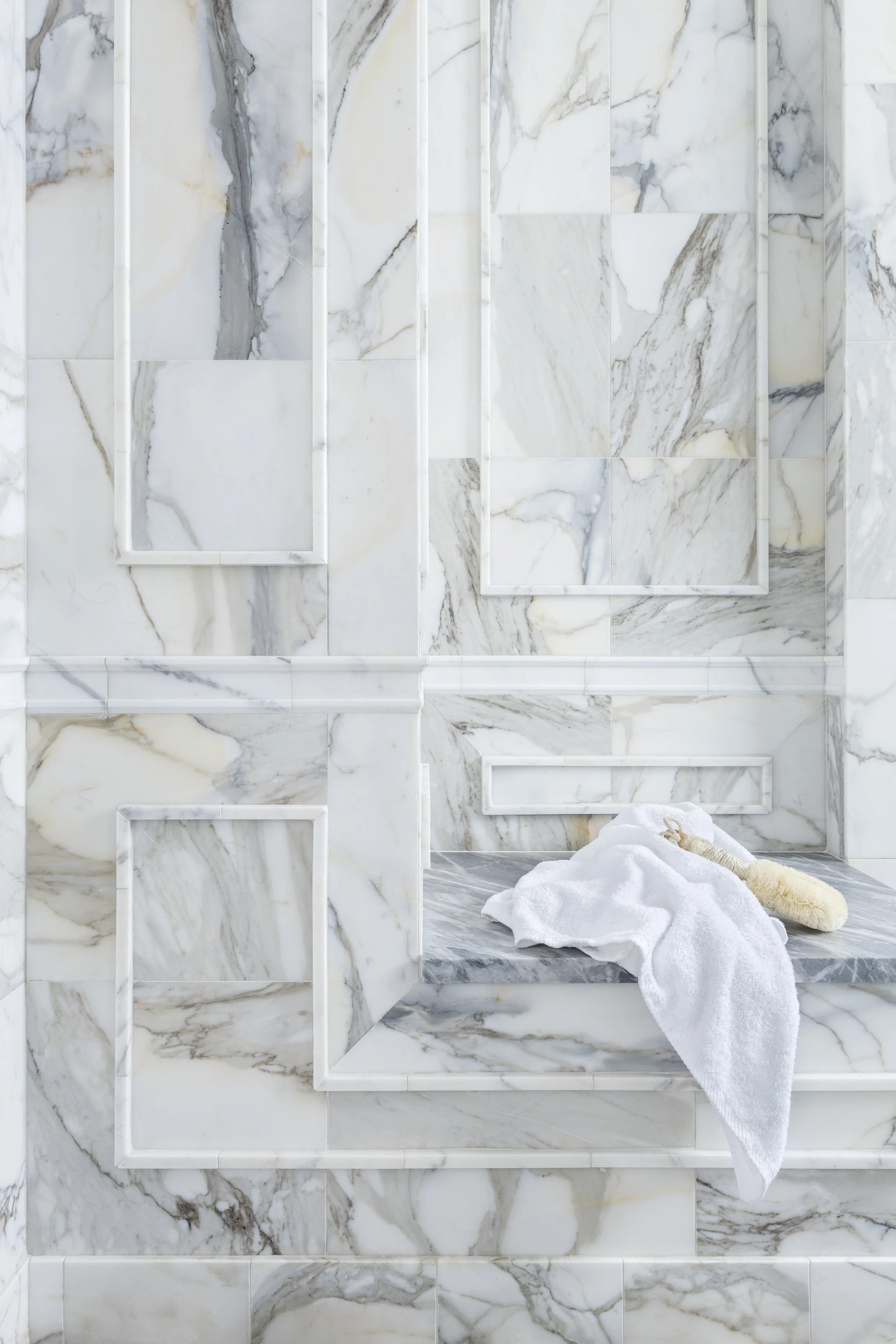 Marble shower wall with integrated niches, stone bench, and folded bath towels.