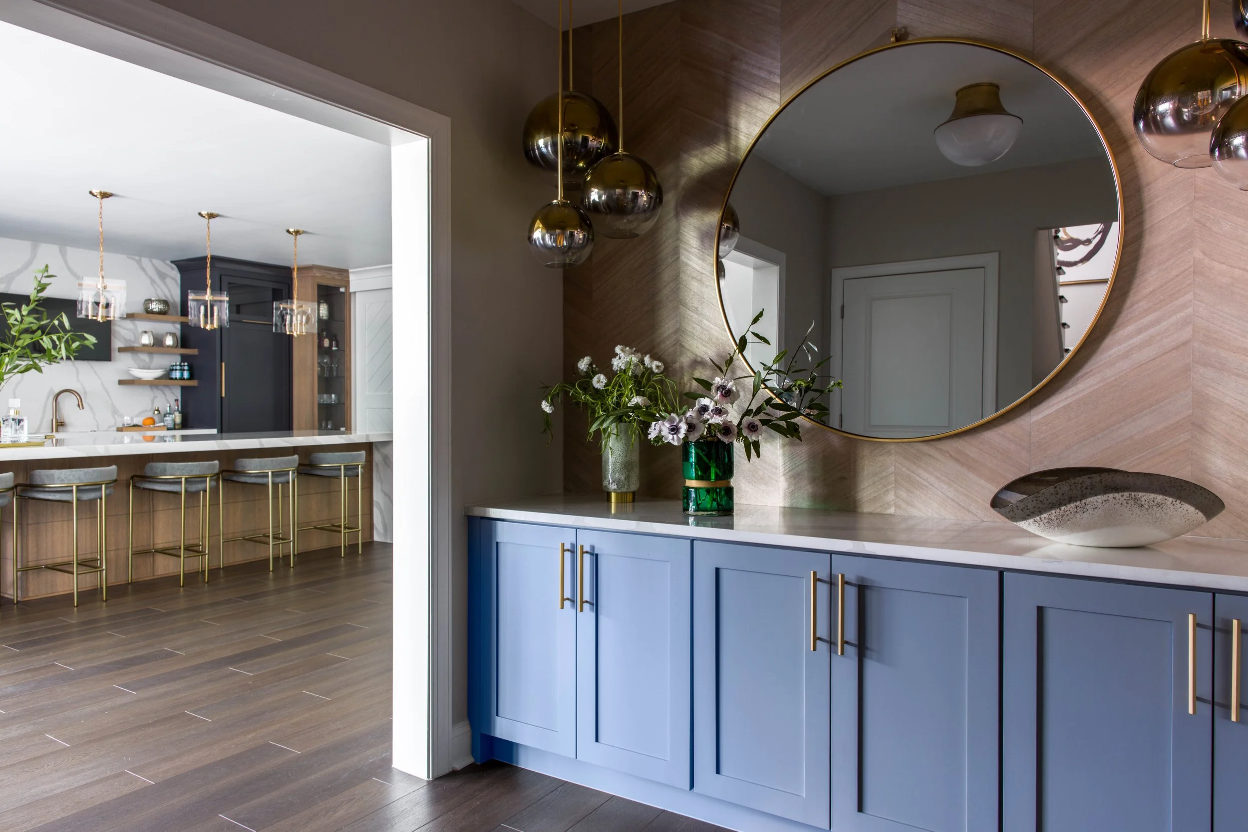 Living space with custom blue cabinetry and brass accents opening into a modern kitchen.