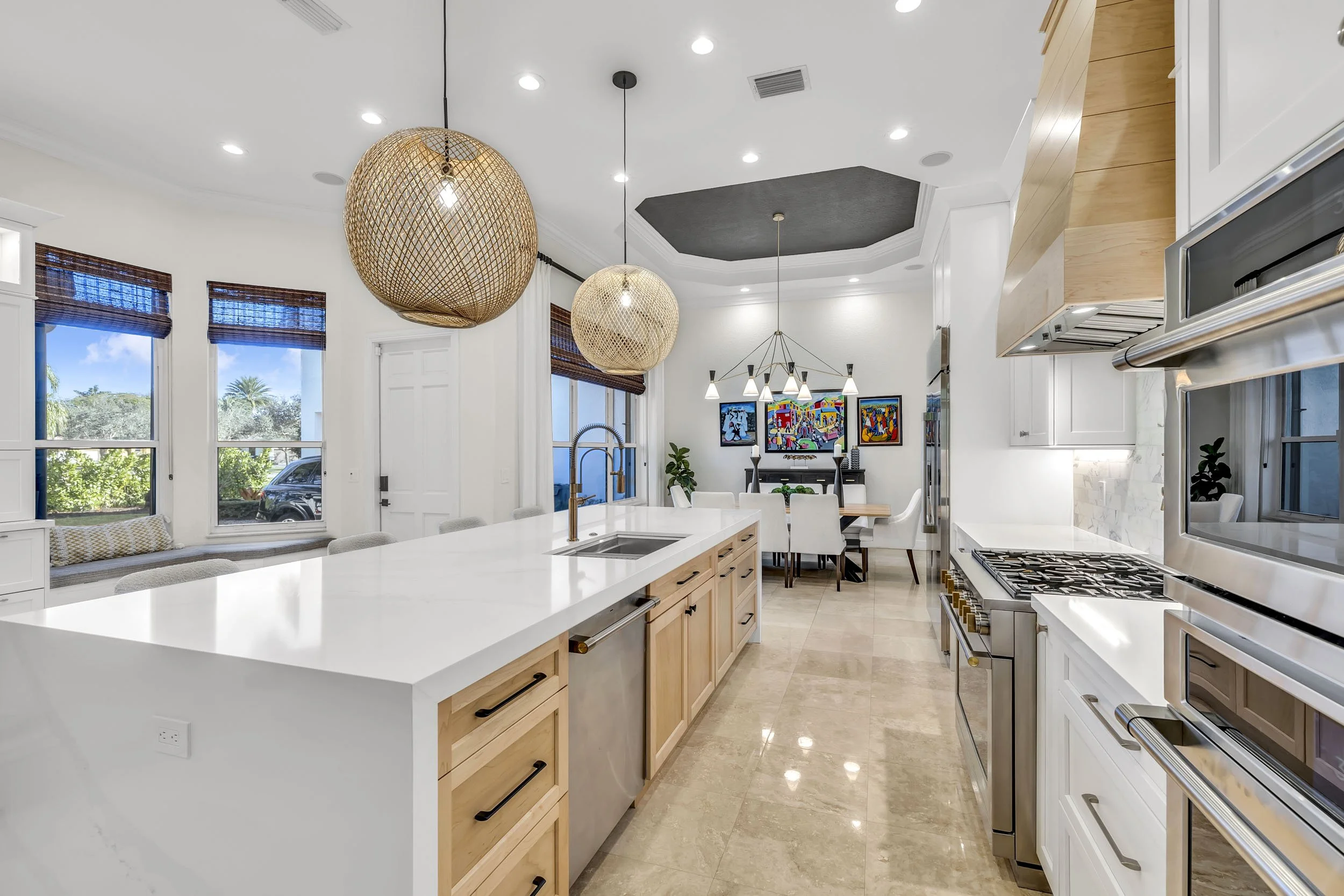 Kitchen showcasing a quartz waterfall edge countertop paired with a 6-burner gas stove and organic woven pendant lighting. Cabinetry blends natural maple finish shaker lowers with white painted shaker uppers for layered texture and visual interest. A