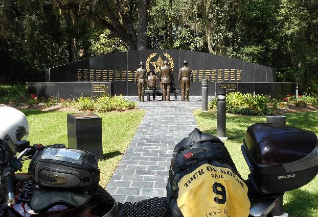 FL1 - Florida Sheriffs Memorial Wall Tallahassee, Florida 2617 Mahan Dr. GPS: 30.456875, -84.233899 Access: 24/7, unrestricted. Parking is available in several adjoining areas, while lining up directly in front of the memorial might be considered ‘high profile.’ Take a photo similar to the one above, along with rider flag and motorcycle. Refer to RULES 5-7 ( http://www.tourofhonor.com/pages/rules.html#rules57 ) for photo verification. Scorers have final say whether standards are met. More.... The Florida Sheriffs Association established this memorial wall in 2002 to honor the heroes of Sheriffs’ Offices killed in the line of duty. Names are added each April for those who died in the previous year. Tallahassee resident and sculptor Sandy Proctor created a sculpture featuring a bench with a group depicting the wife of a fallen deputy, her small child, a sheriff and fellow deputies facing the curved marble wall engraved with the names of the fallen officers. 