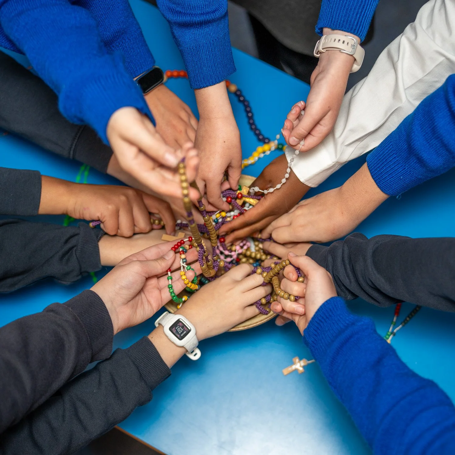 Childrens hands reaching towards prayer beads and rosaries at Ladymount Catholic Primary School