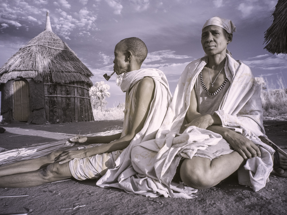 Elderly Nuer couple outside their hut at dawn.