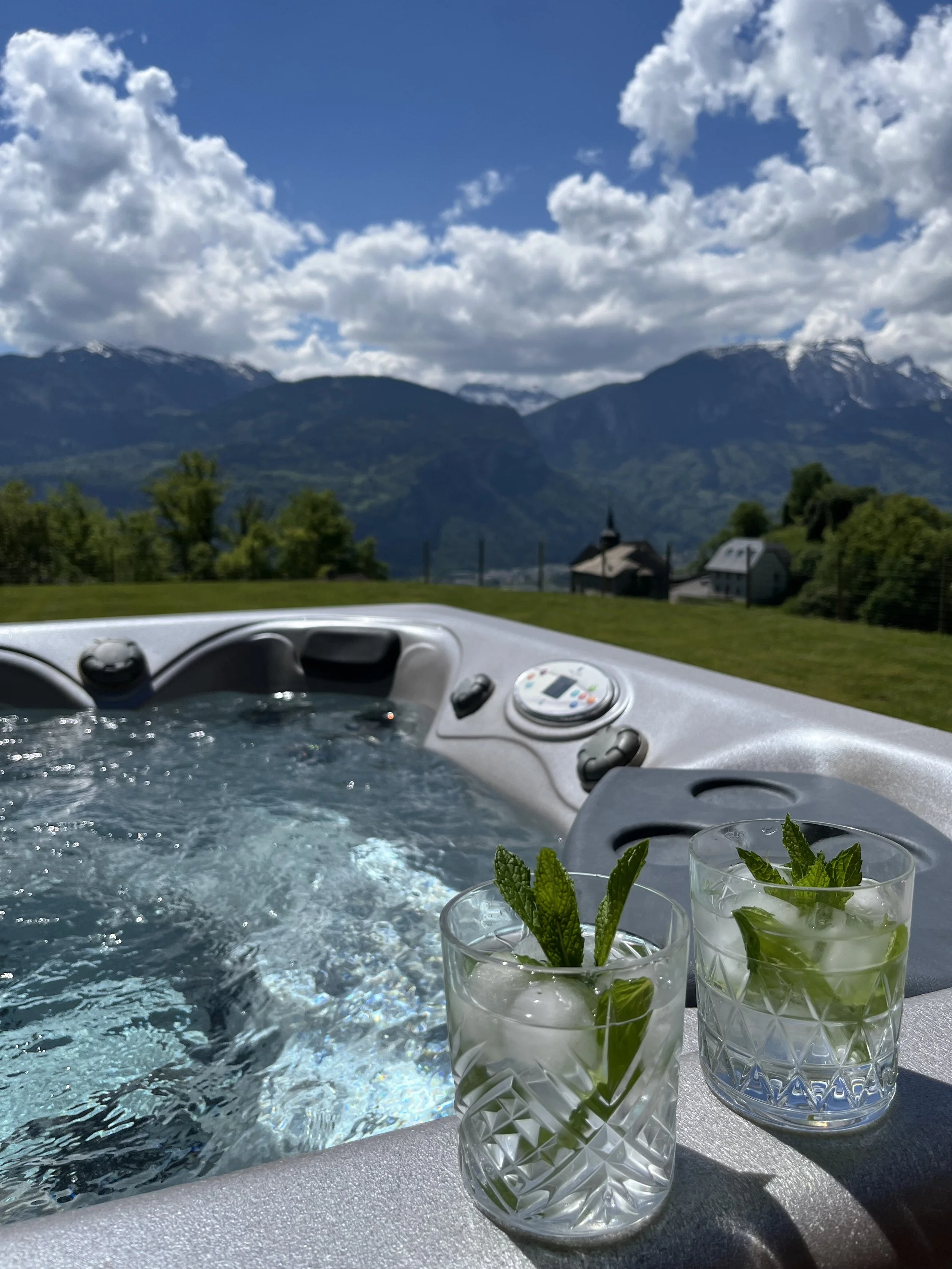 a view from the hot tub over the Aravis Mountains in the distance, two glasses of gin & tonic sit on the side of the hot tub