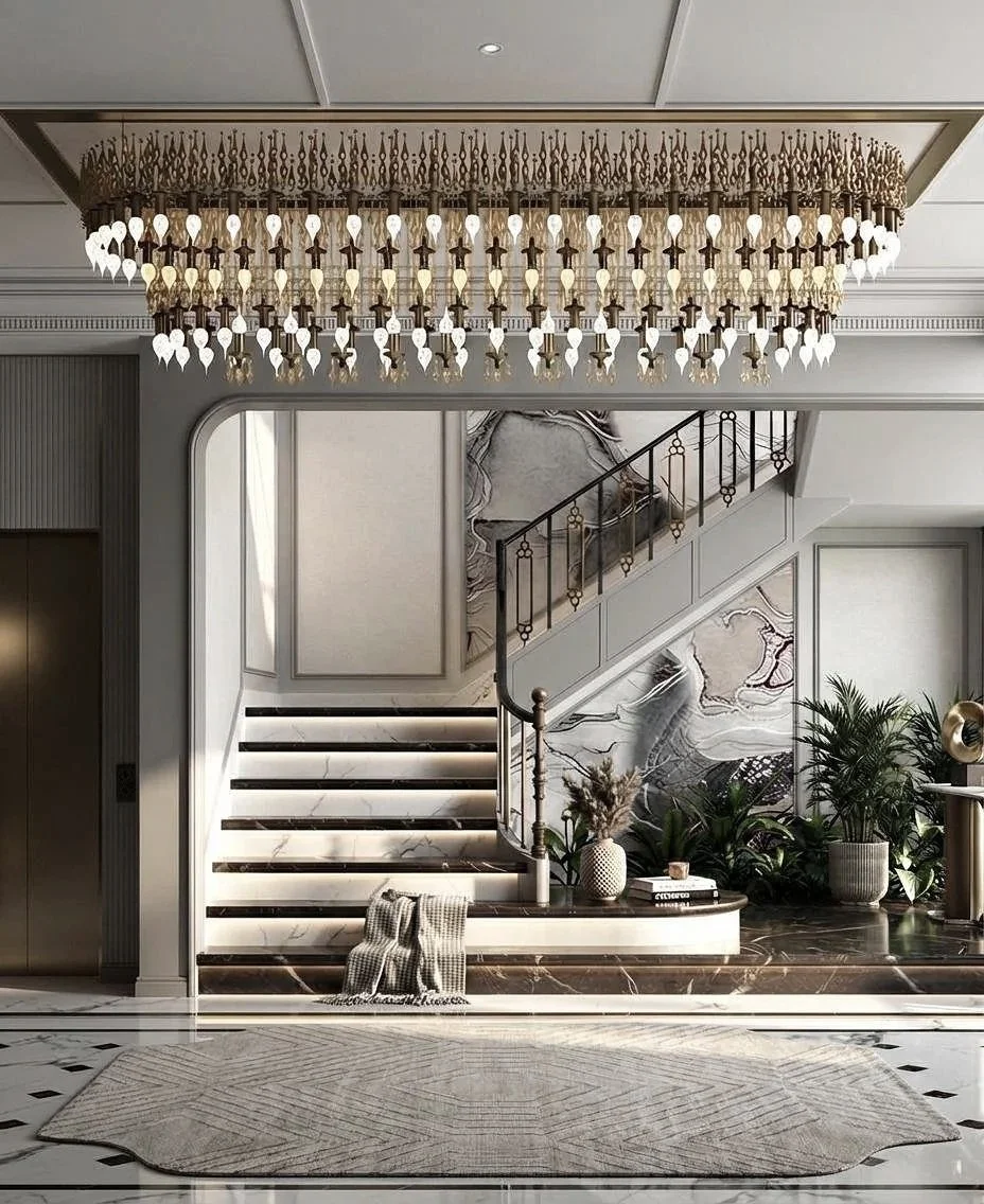 Luxurious hotel lobby with a marble staircase, modern rug, large chandelier, and decorative plants.