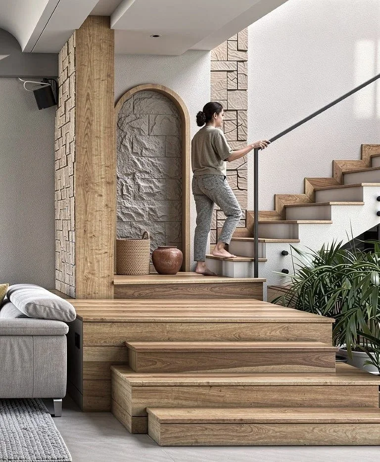 A woman ascending wooden stairs inside a modern home, surrounded by textured walls, plants, and decorative pottery.