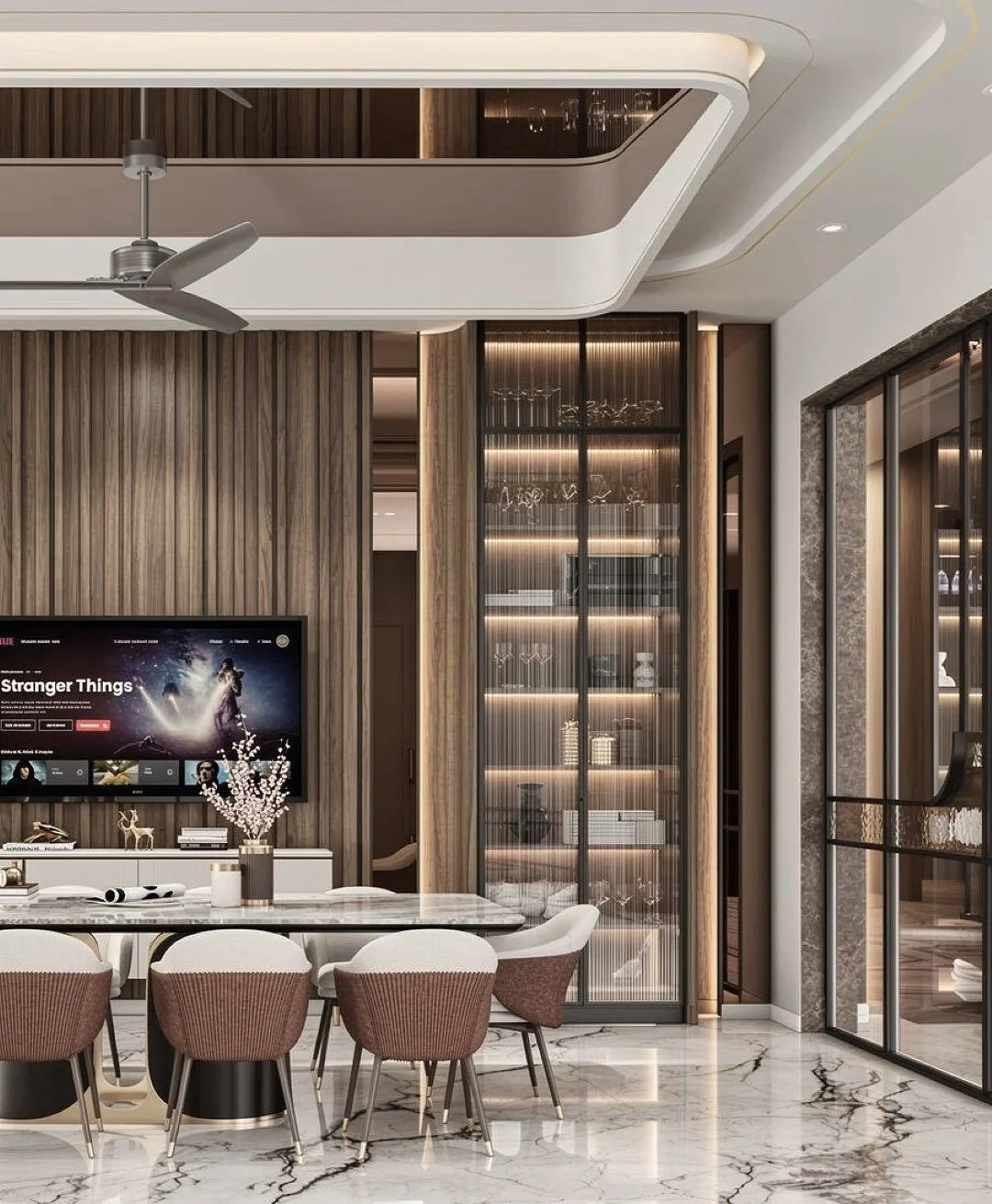Modern dining room with a white marble table, light brown chairs, a wall-mounted TV showing "Stranger Things," and a large wooden display cabinet with glass doors and illuminated shelves.