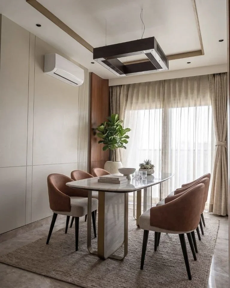 Modern dining room with a rectangular marble table, six upholstered chairs, a large window with sheer curtains, a potted plant, and a ceiling-mounted air conditioning unit.