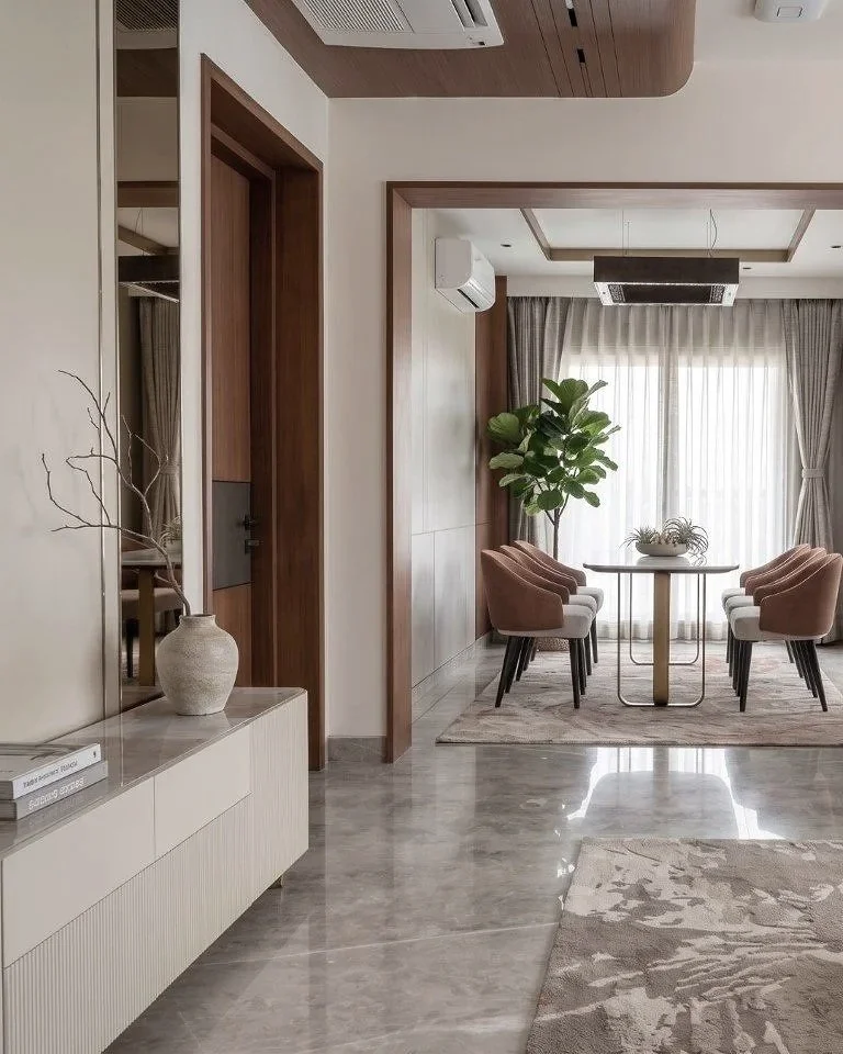 Elegant dining area with six pink upholstered chairs around a round table, large window with sheer curtains, potted plant, and modern decor.