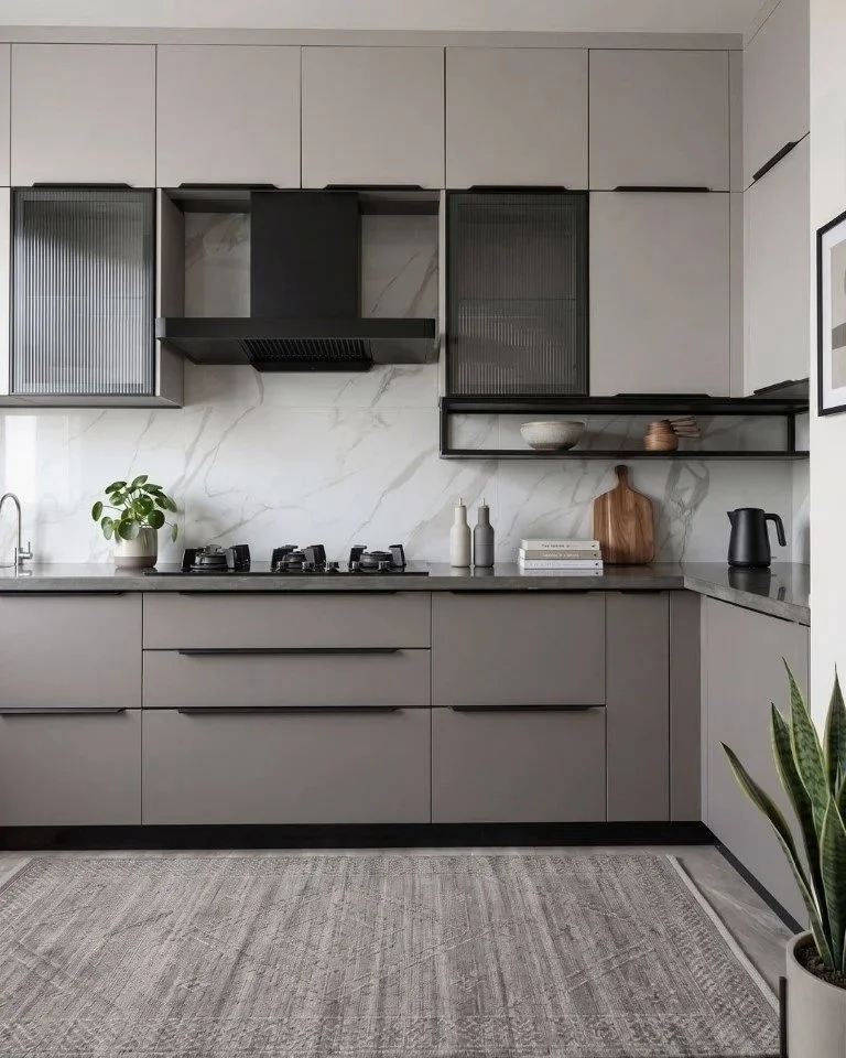 Modern kitchen with gray cabinets, marble backsplash, black open shelf, potted plant, books, decorative vases, cutting board, black electric kettle, and a snake plant in the corner.