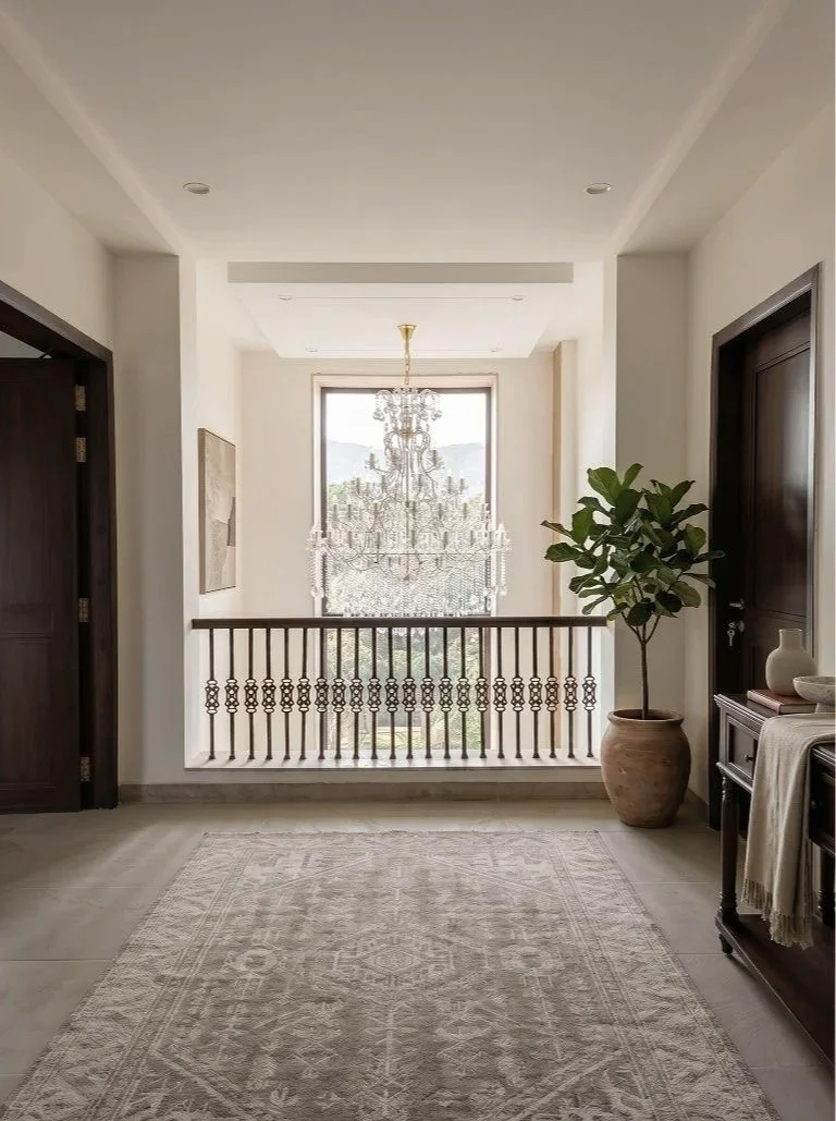 Interior view of a bright hallway with a large window, chandelier, potted plant, and wooden doors.