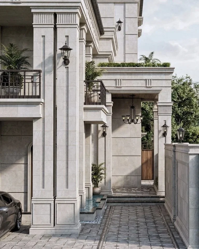 Front of a large, elegant residential building with stone facades, plants, and decorative lighting, featuring a driveway and an entry gate.