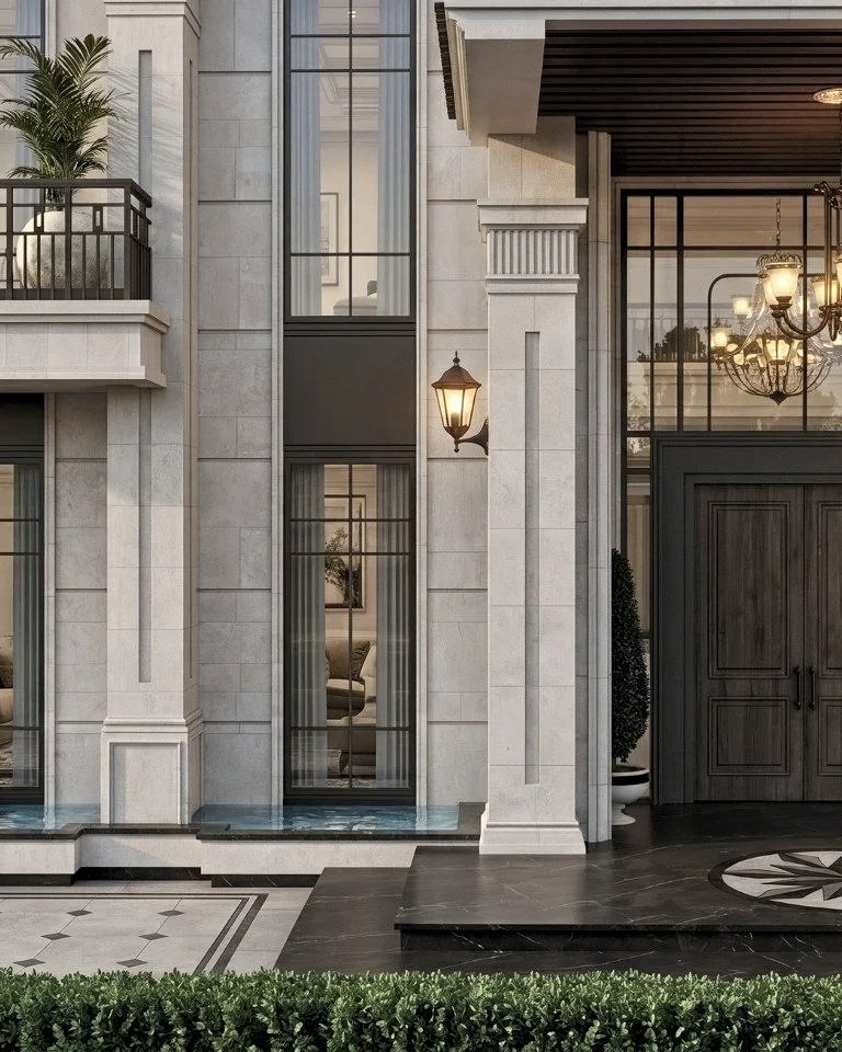 Exterior of an upscale building with large glass windows, a wooden door, stone walls, a balcony with plants, a lit lantern, and an elegant chandelier inside visible through the windows.