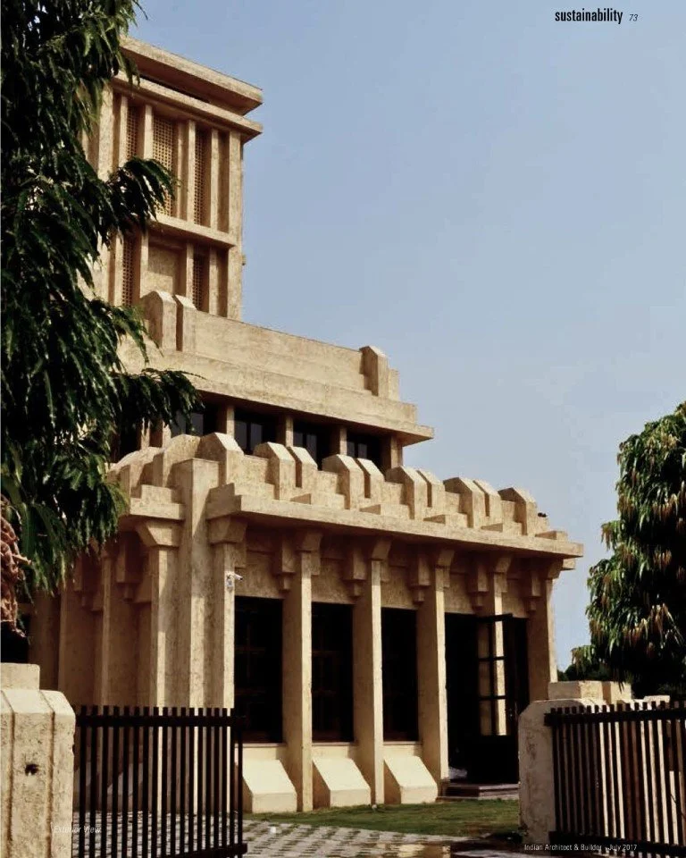 A modern building with Art Deco architectural style, featuring geometric shapes, columns, and decorative details, partially obscured by green trees.