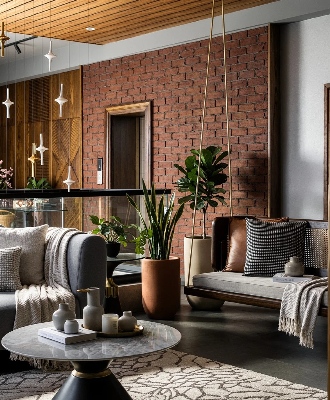 Modern living room featuring a blue sofa with pillows, potted plants, a patterned rug, a black TV stand with shelves, and a decorative chandelier hanging from a wooden ceiling.