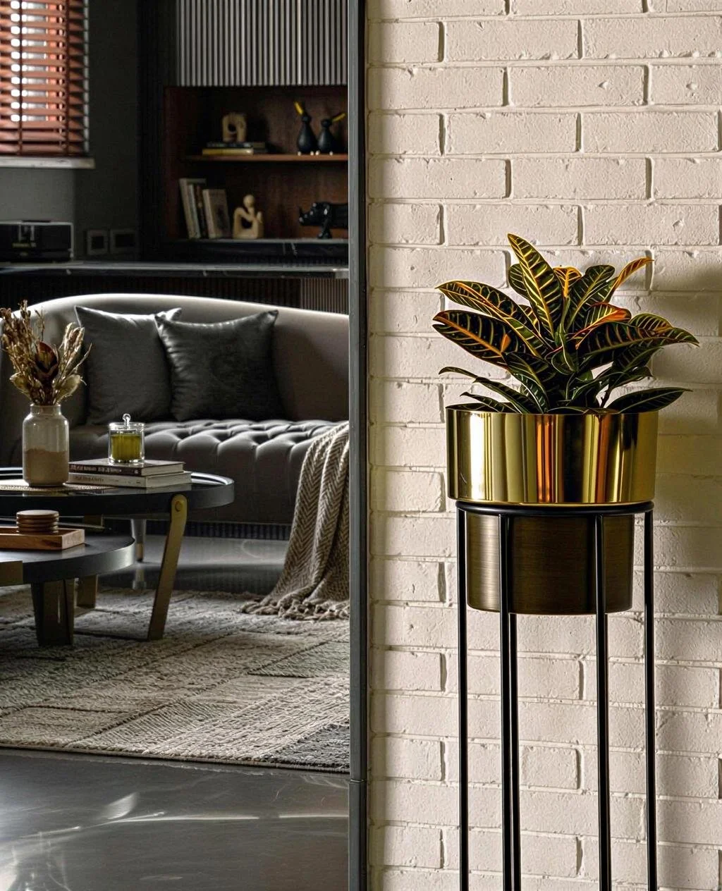 A gallery wall with a sofa and decor in a living room on the left side; a modern potted plant in a metallic gold planter on a tall black stand against a white brick wall on the right side.